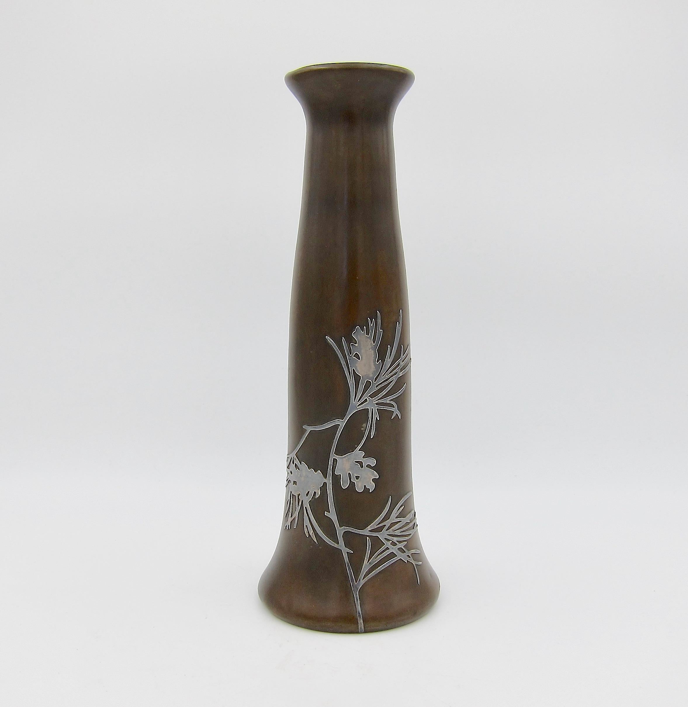 An American Arts & Crafts bronze vase with a sterling silver pine branch overlay from Heintz Art Metal Shop of Buffalo, New York, dating circa 1915. The vase has a tapering cylindrical body with a flared base and mouth and a rich brown patina