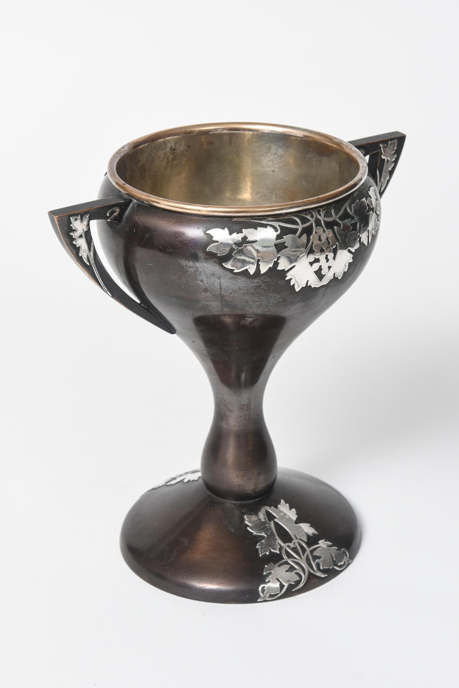 Early 20th century Arts & Crafts mixed metals trophy probably made by Heintz Art Metal Co. This beautiful bronze double handled loving cup has a gorgeous sterling silver overlay grape vine leaf design. The base, arms and peak of cup on the front as
