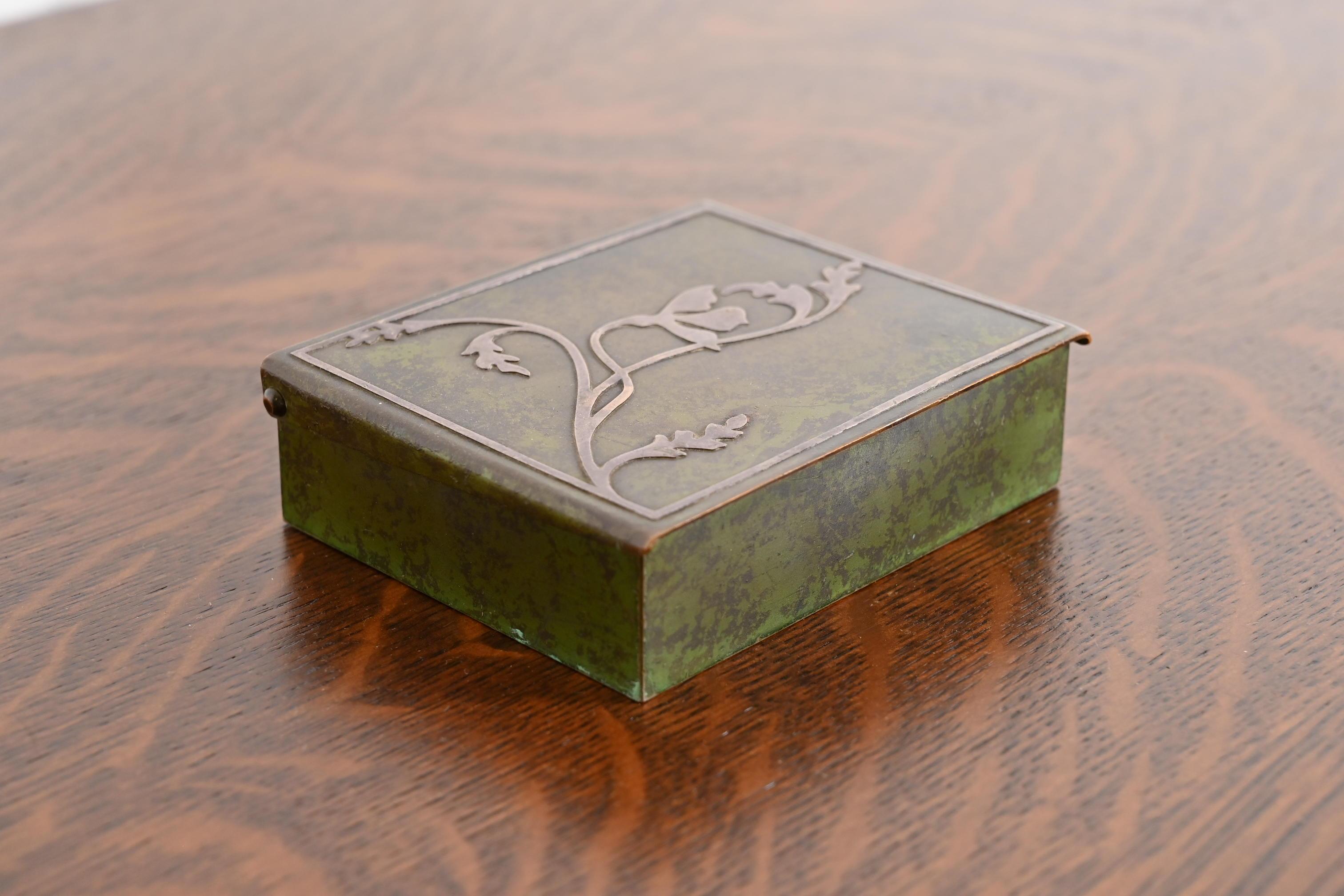 Preciosa caja de escritorio, humidor o cigarrera de la época Arts & Crafts con pátina verde verdigris

Por Heintz Art Metal Shop

EE.UU., principios del siglo XX

Plata de ley sobre bronce, con interior forrado de cedro.

Medidas: 4,25