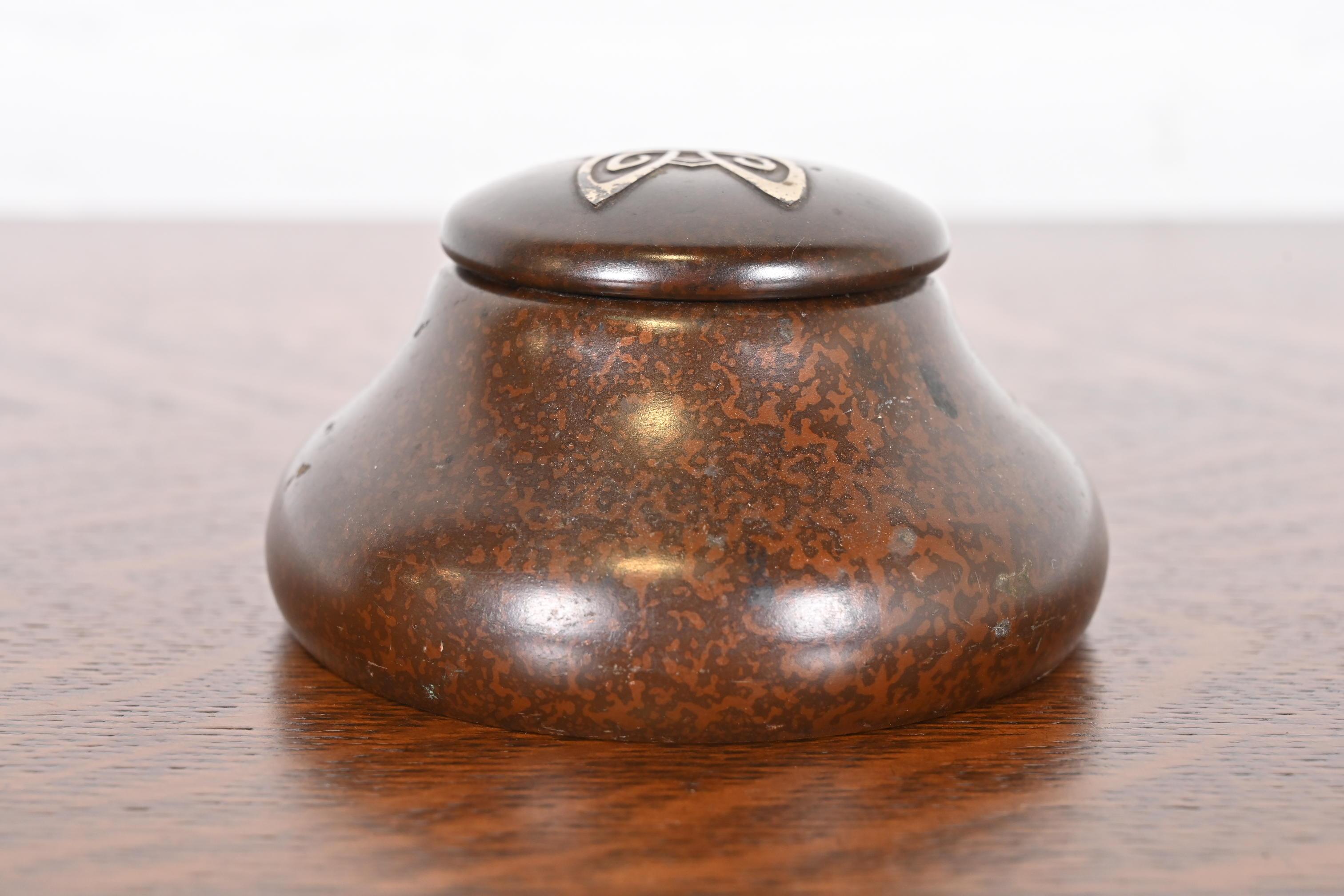 A gorgeous Arts & Crafts period bronze inkwell with sterling silver inlay design

By Heintz Art Metal Shop

USA, Early 20th Century

Patinated bronze, with sterling silver inlay.

Measures: 4.25