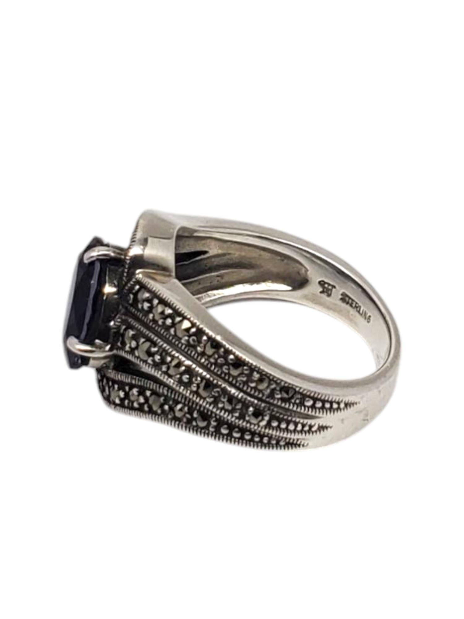 Anello con pietra viola e marcasite in argento sterling Heirloom 73 -

Questo anello vintage in argento sterling presenta una pietra viola di forma ovale (10 mm x 7,8 mm) incastonata in una fascia ornata con accenti di marcasite di A. Silver