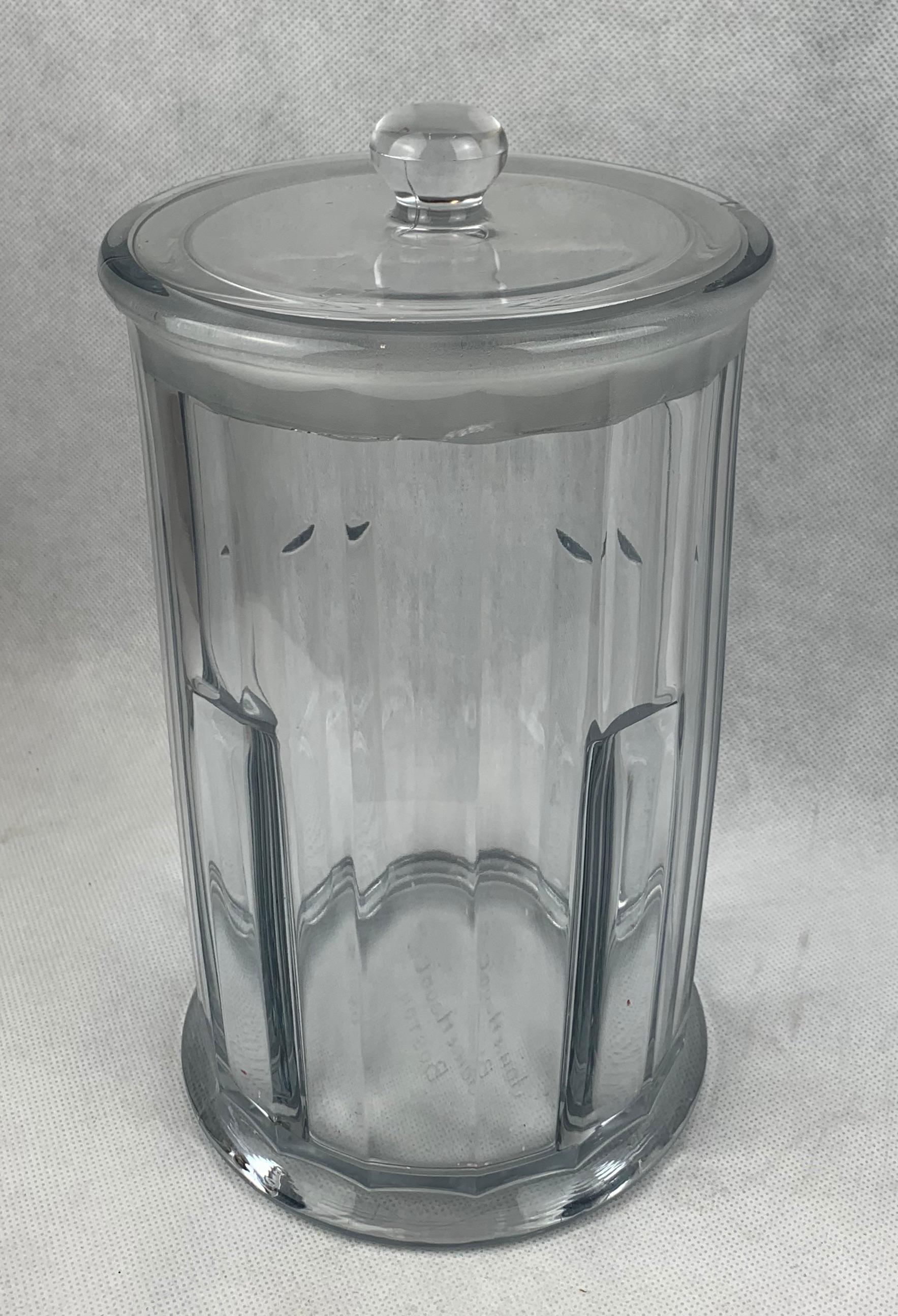 Heisey Glass created this glass apothecary jar with cover for John Hood Co., Boston early in the twentieth century. This thick glass piece has twelve faceted panels and a ground glass stopper. The stopper has some chips due to the nature of its use.