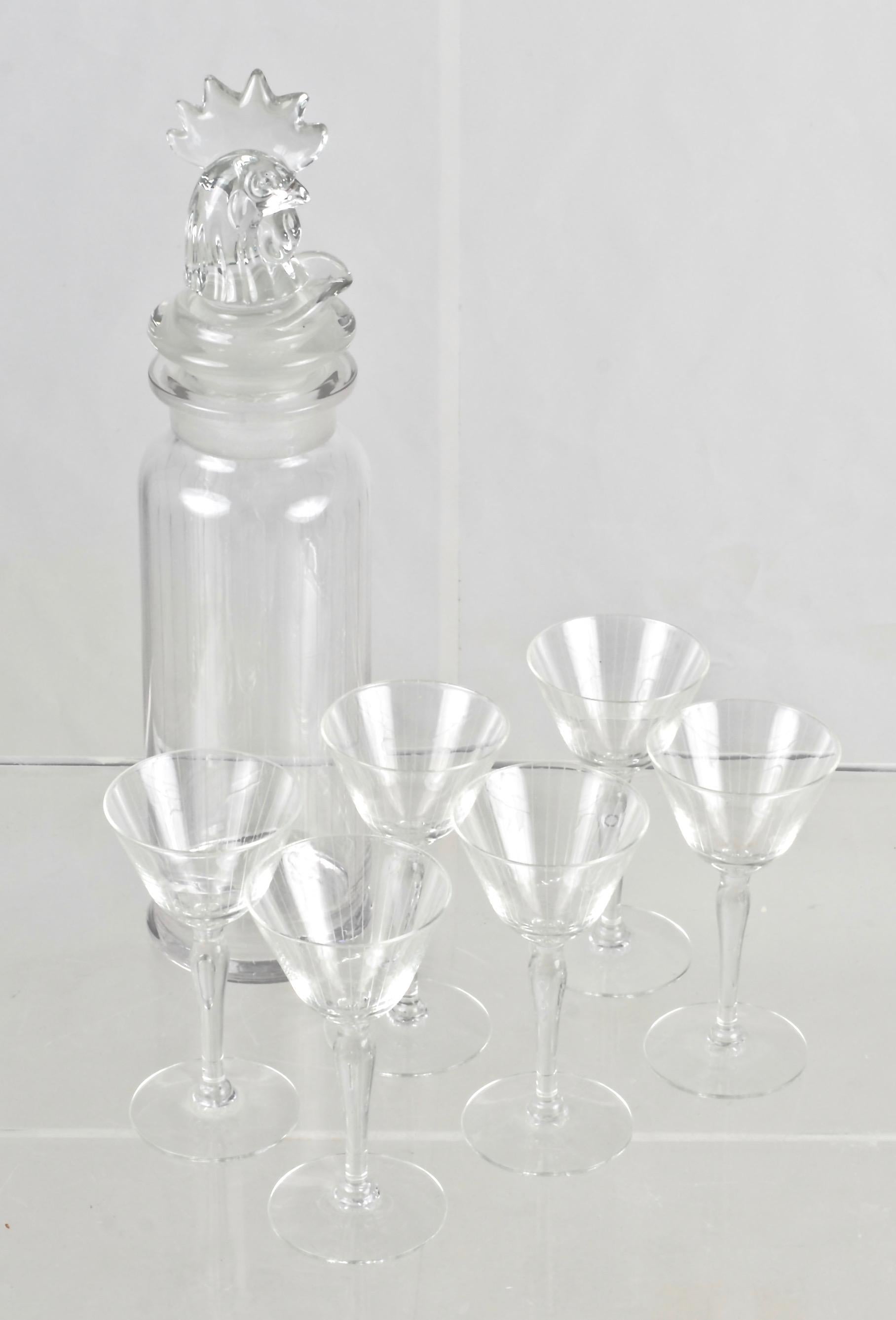 Signed Heisey glass cocktail shaker with finely figured rooster top resting in pouring spout with perforations. Subtle vertical stripe detail incised on both the shaker and the cocktail glasses. Five cocktail glasses in set. Shaker measures 3.5