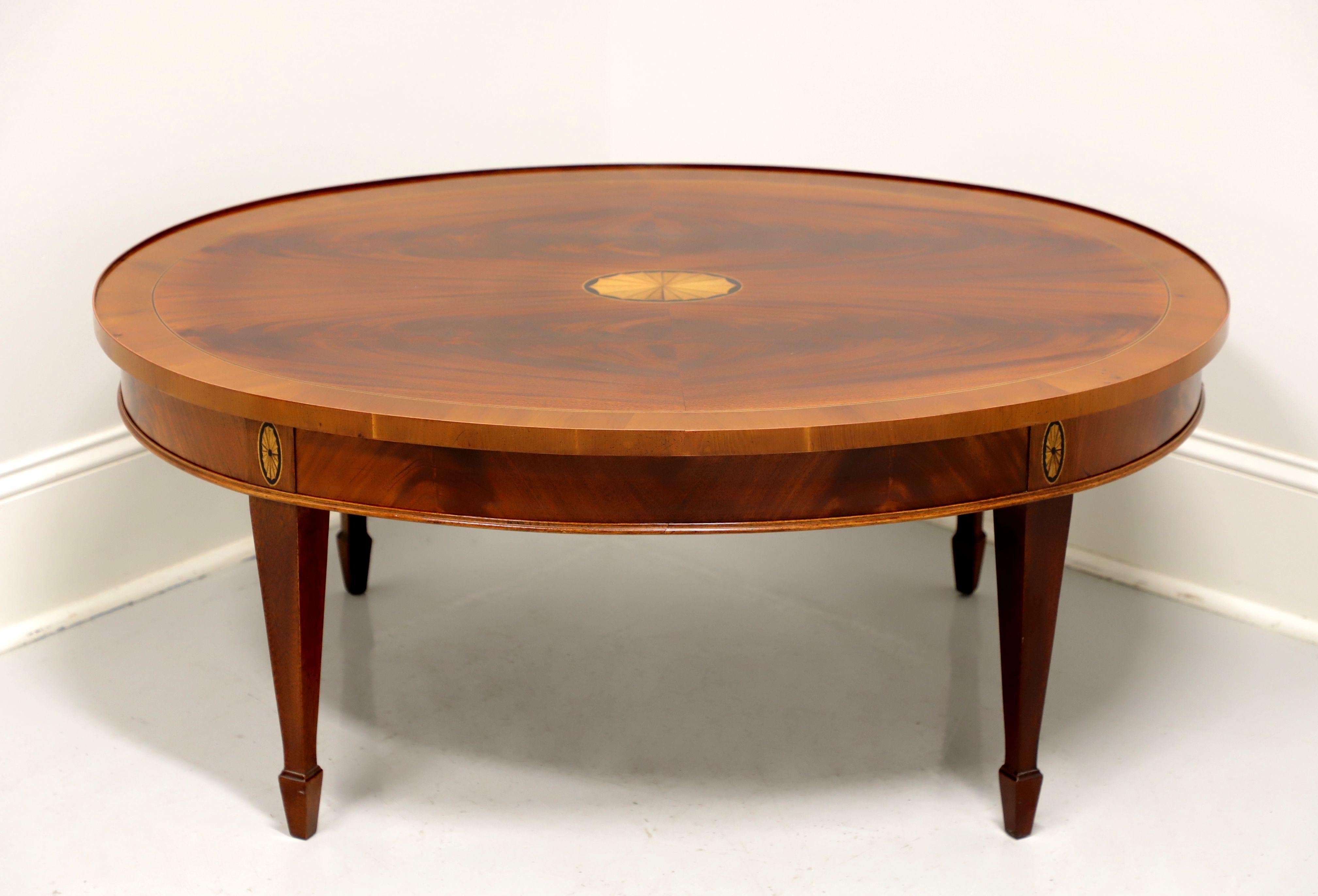 A Georgian style oval coffee table by Hekman Furniture, from their Copley Place Collection. Mahogany, flame mahogany and yew wood with banded & inlaid top, inlaid apron, tapered legs and spade feet. Made in North Carolina, USA, in the late 20th
