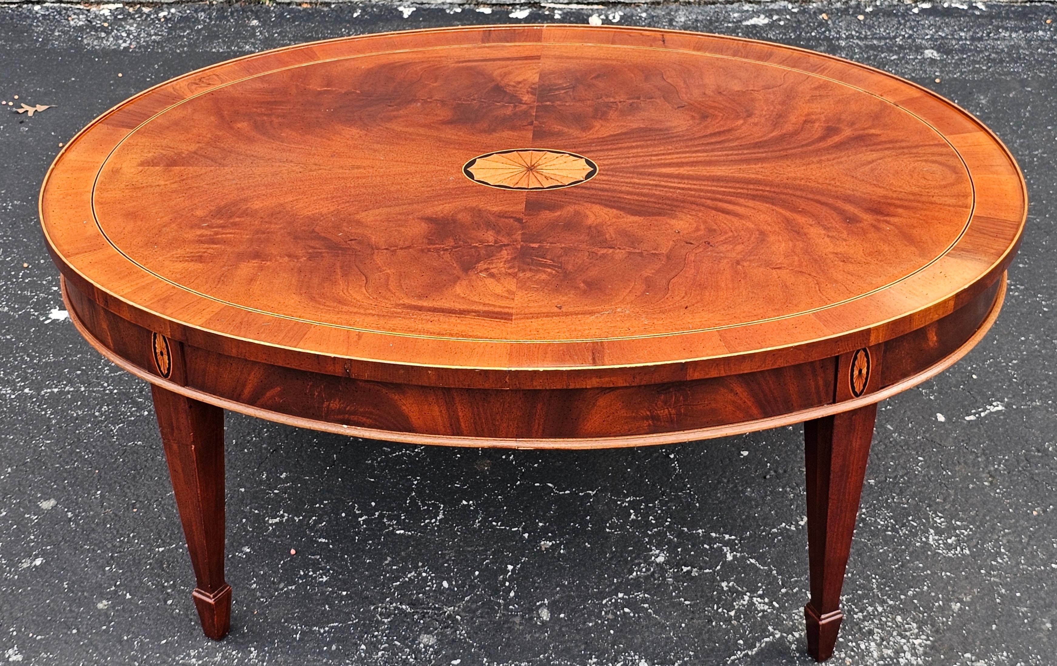 Esta mesa de centro presenta sólidos de caoba con un borde de madera de tejo y una inserción de remolino de caoba en la parte superior. También tiene incrustaciones de marquetería en el centro de la encimera y en las patas, con detalles de