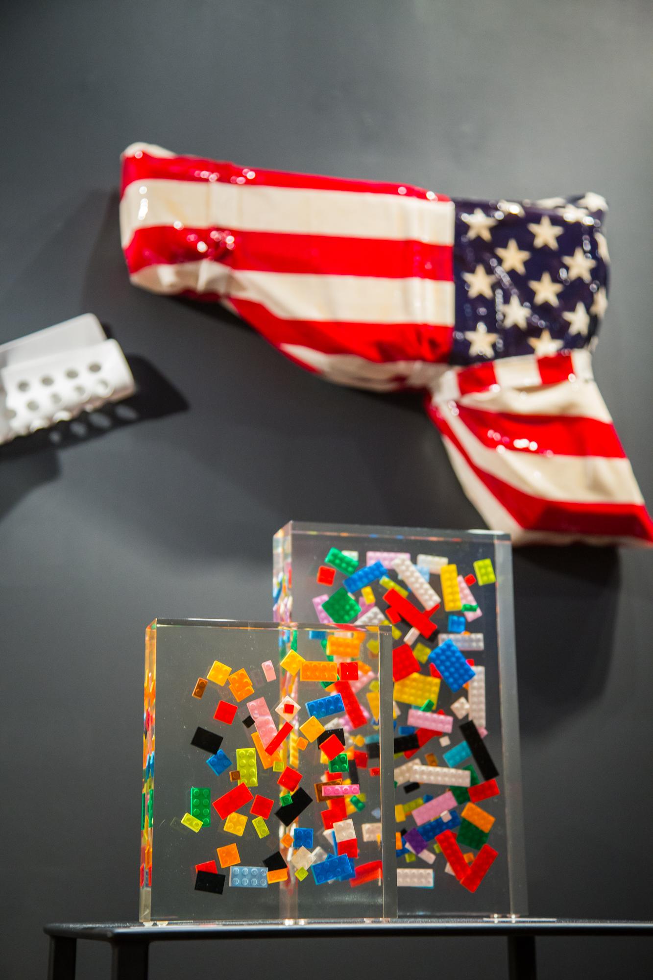 American Flag in the form of a revolver sealed with fiber resin. The flag has eye hooks on the back so that it can be mounted on the wall. Edition 1 of 8. 

  About the Artist Helder Batista is a self-taught artist who works predominantly in