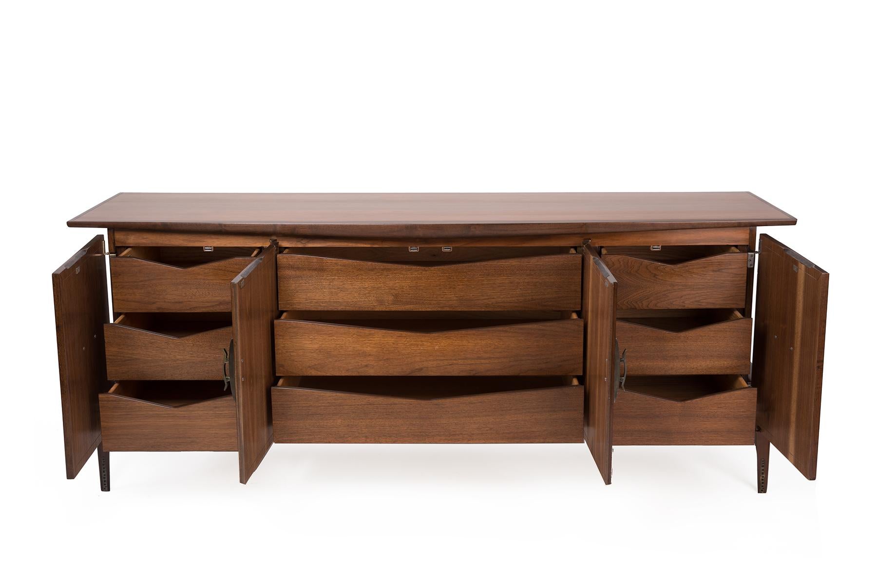 Newly finished walnut credenza by Helen Hobey for Baker. This example features formed bronze pulls, sculptural forms and plenty of interior storage. We also have a matching set of nightstands available.