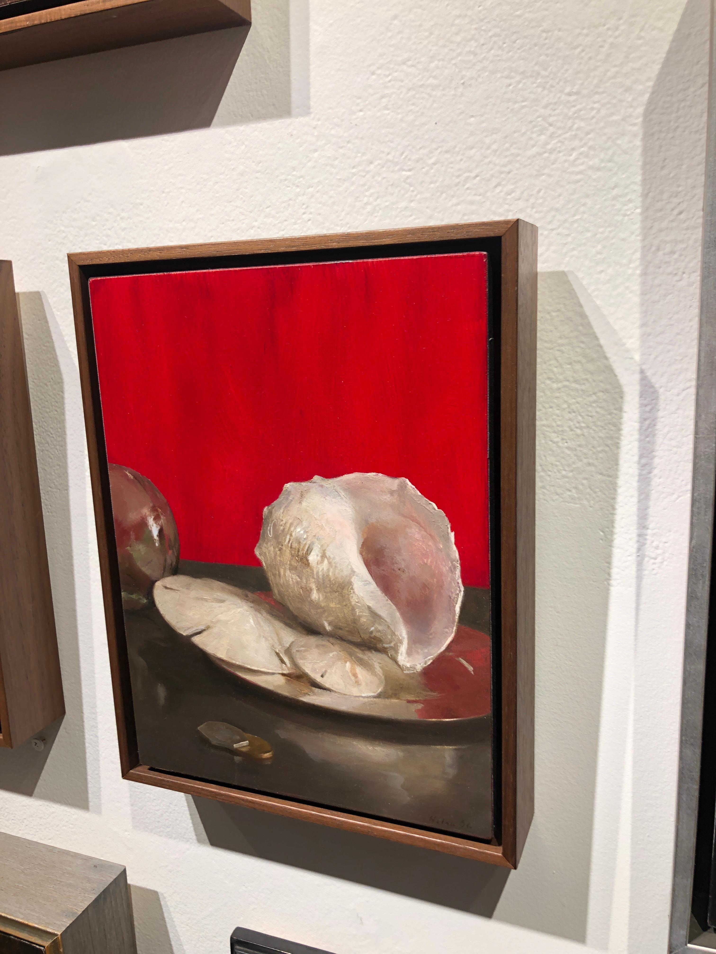 The inherently beautiful sand dollars and sea shells are arranged on a silver tray and flanked by coins and a reflective orb. The background is a vibrant red reflecting itself on the edge of the silver tray.  This artwork is framed in a simple