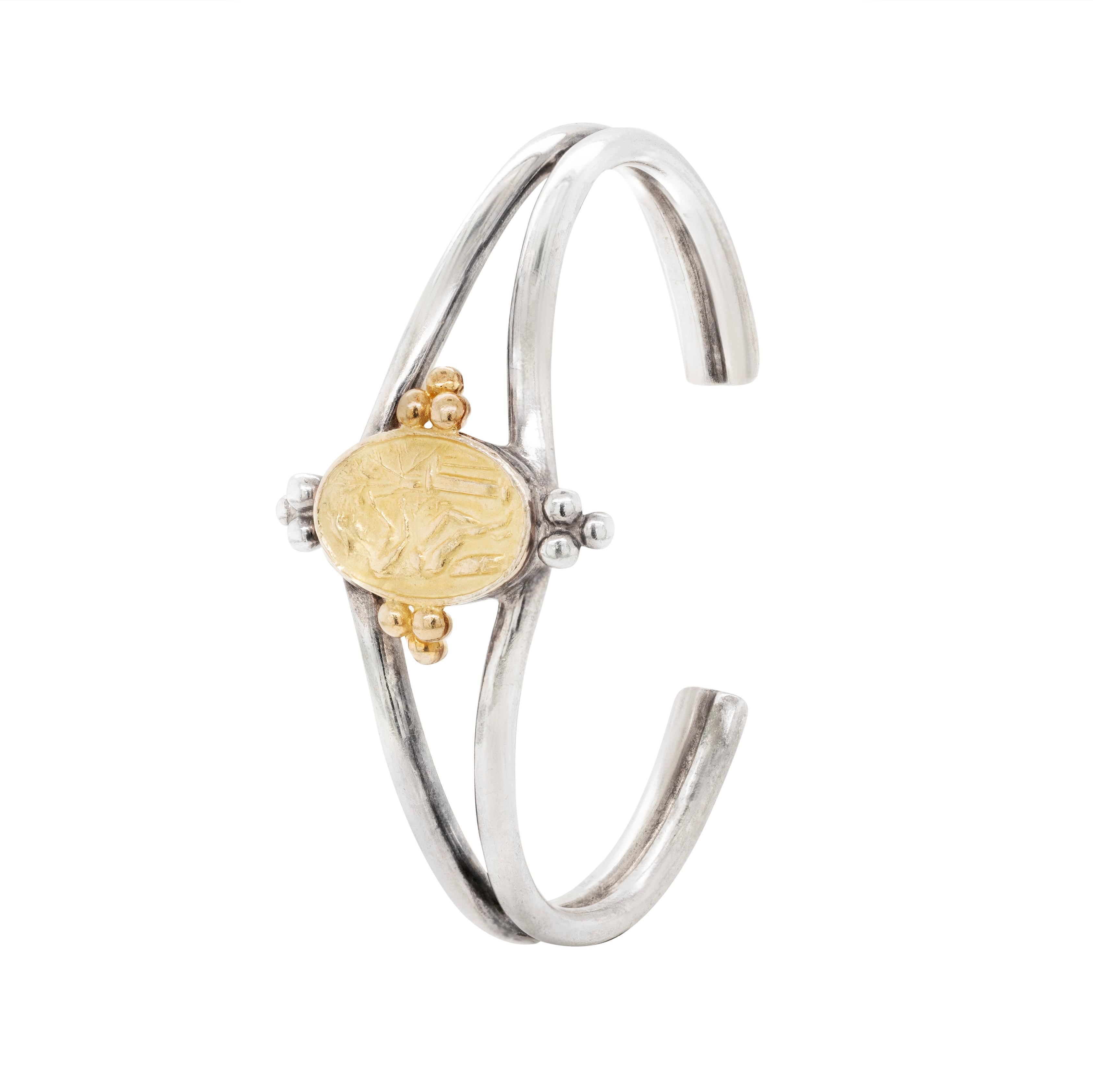 This wonderful piece by famous designer Helen Woodhull is beautifully designed as a split cuff with soldered ends masterfully crafted from sterling silver and 22 carat yellow gold. The centerpiece is a 22 carat yellow gold oval shaped intaglio