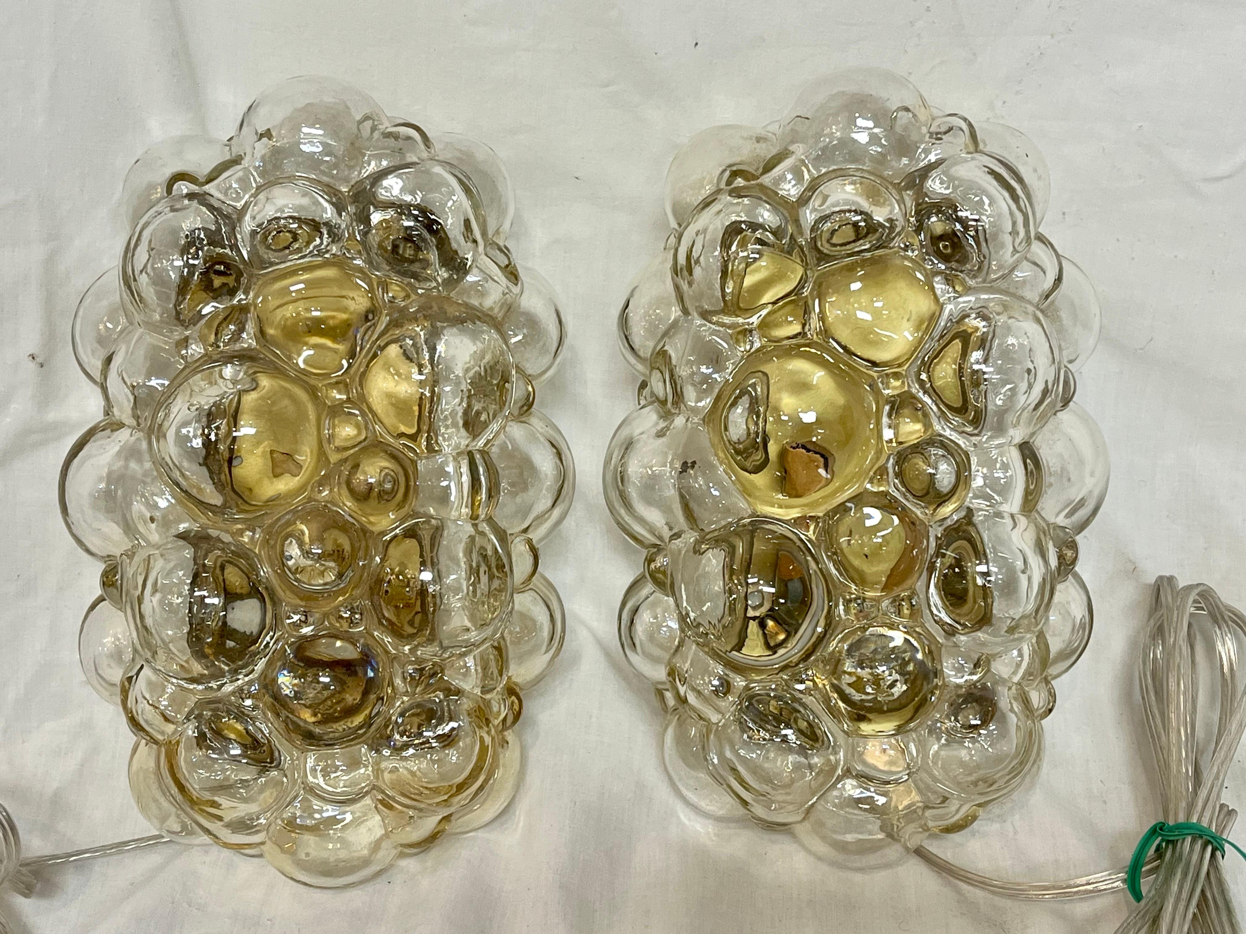 A truly magnificent pair of Helena Tynell for Glashutte Limburg wall sconce lights in a champagne / amber color. The bubble glass is clear with the champagne / amber hue. On the original brass mounting boxes with the original screws, this pair has