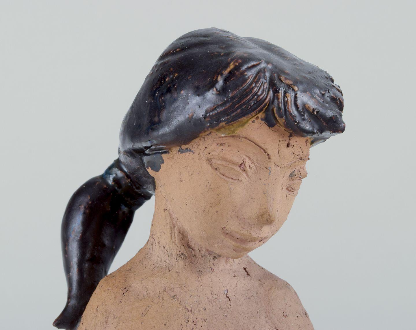 Helge Christoffersen (1925-1965), laboratorio personale.
Figura unica in ceramica di una giovane donna nuda con un panno. 
Terracotta parzialmente smaltata.
Smalto nei colori marrone-verde, marrone e blu.
Datazione: Metà del XX secolo.
Firmato in