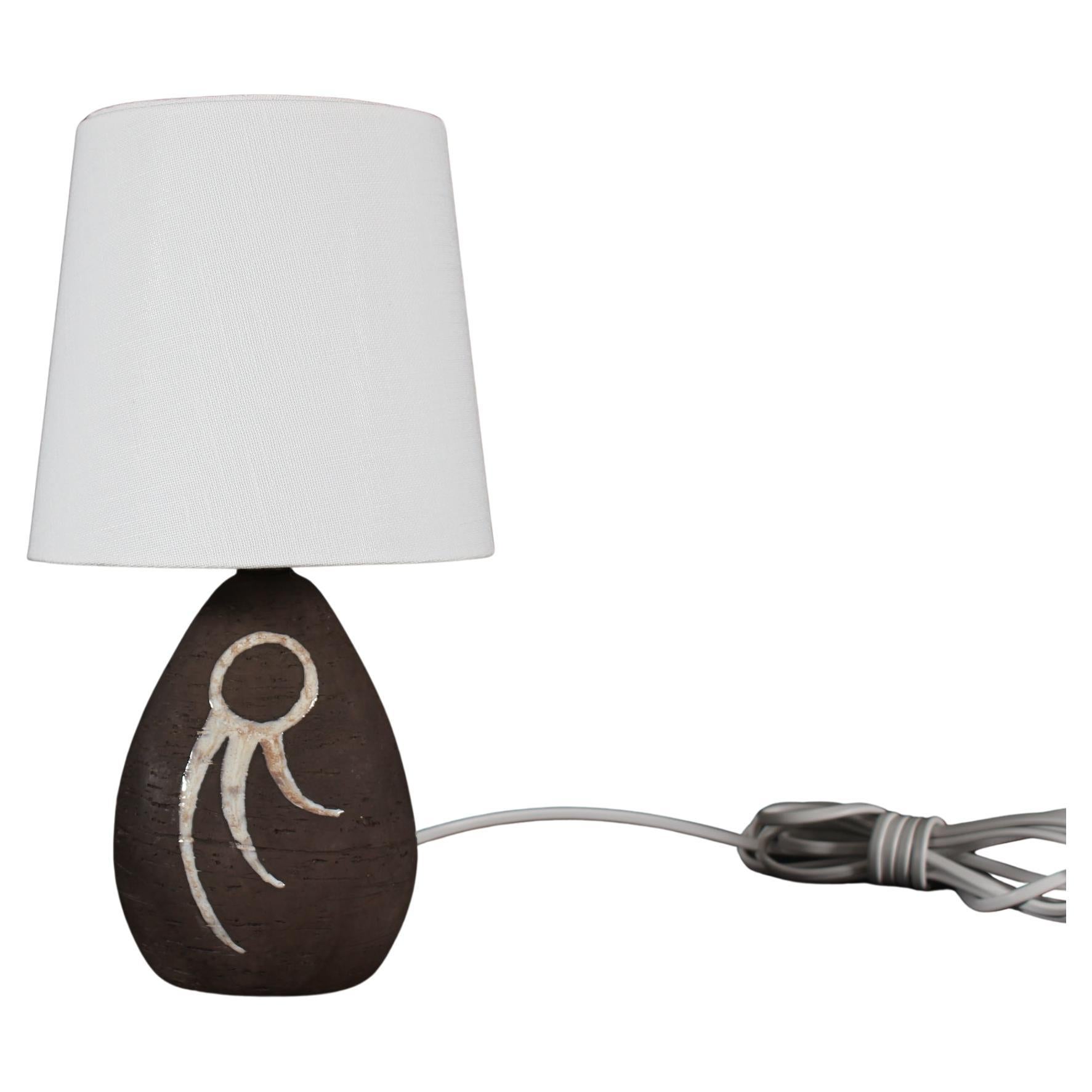 Bedside- and table lamp by ceramist Helge Østerberg (1905-1982) made at his own workshop.

The triangular shaped base of chamotte clay is left unglazed apart from an abstract white decoration with a speck of brown.

Included is a new clip-on bulb