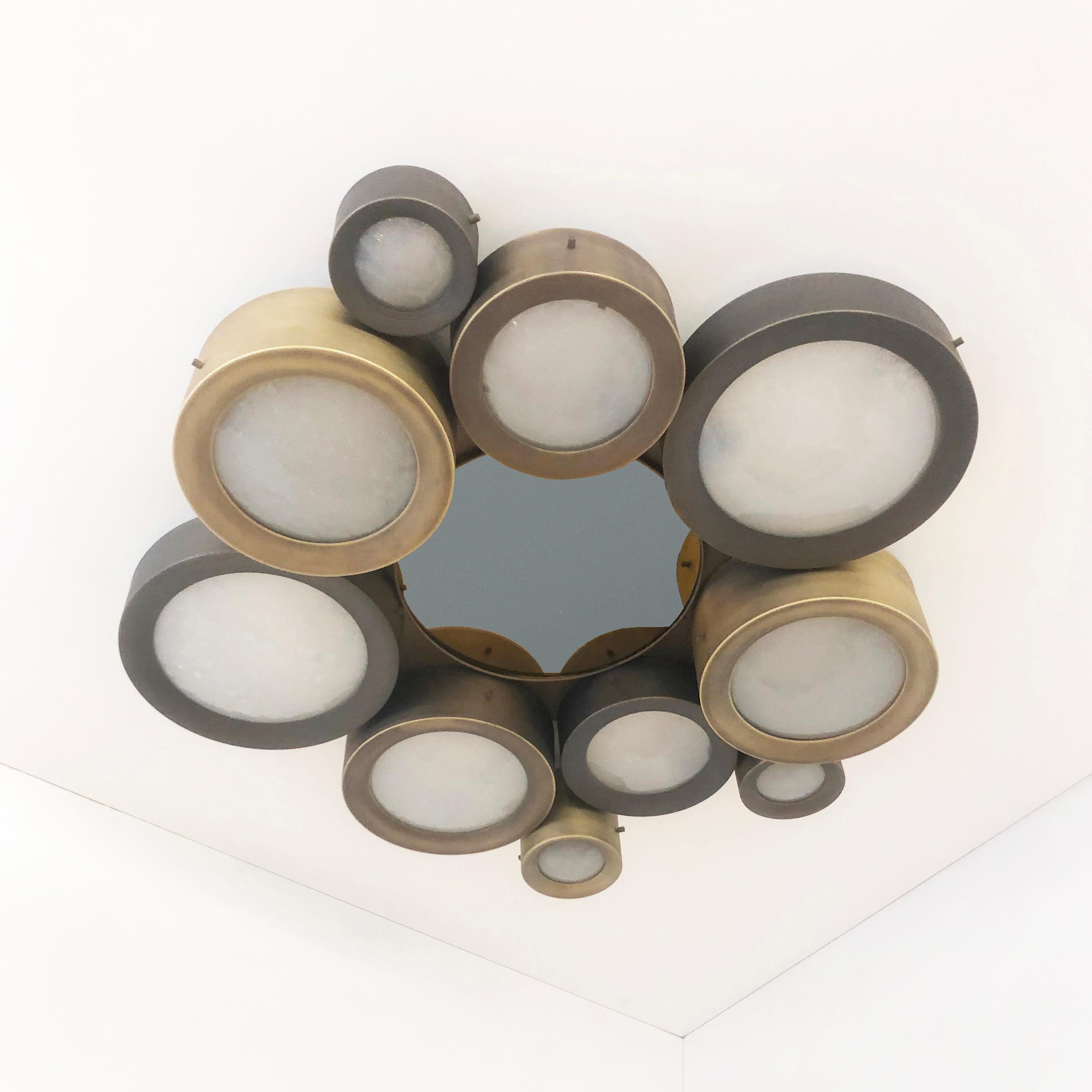 The Helios ceiling light features an imposing composition of illuminated Murano glass shades gravitating around a central tinted mirror. The first images show the fixture in a medley of bronze finishes with a gray center mirror-subsequent pictures