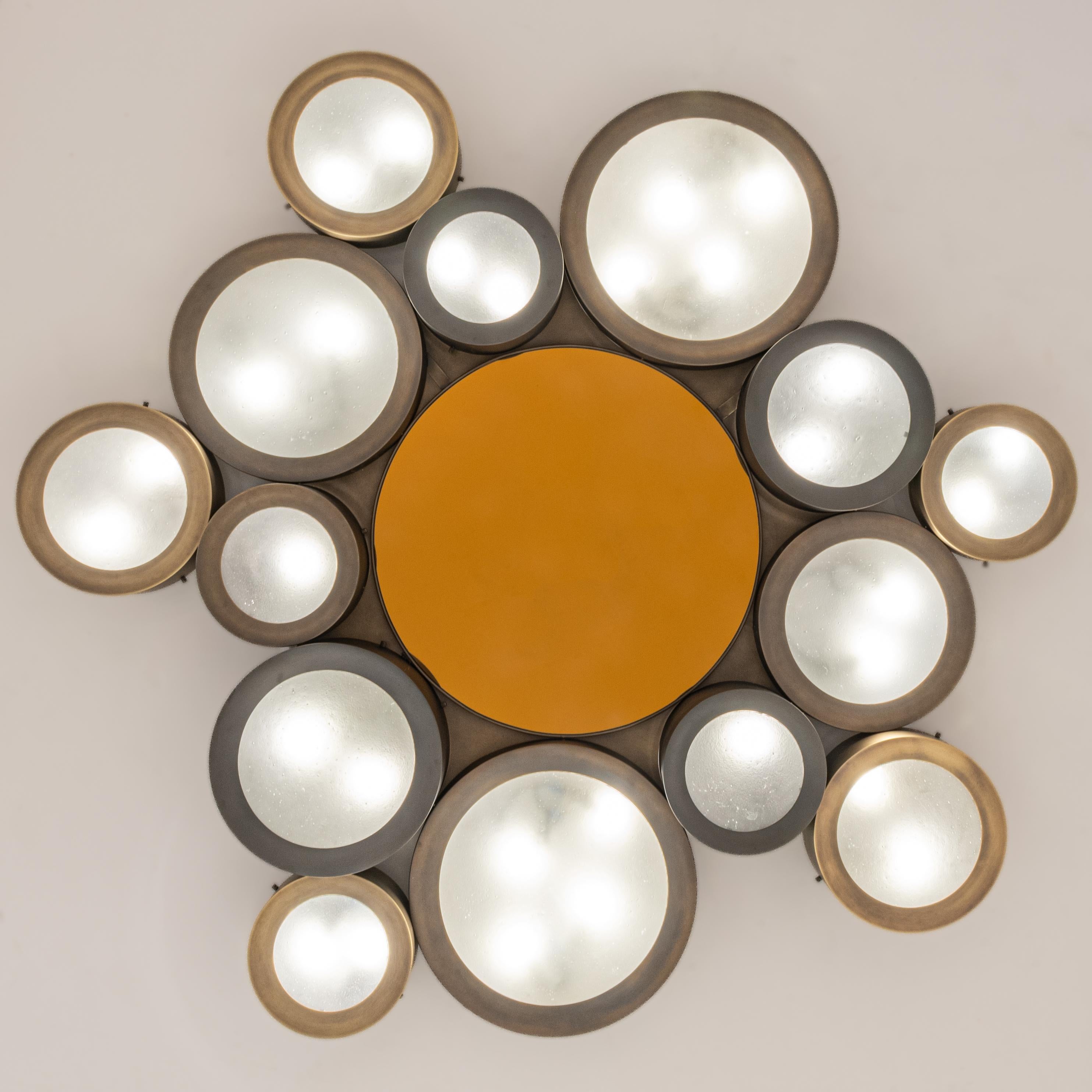 The Helios ceiling light features an imposing composition of illuminated Murano glass shades gravitating around a central tinted mirror. The first images show the fixture in a medley of bronze finishes with an amber center mirror-subsequent pictures