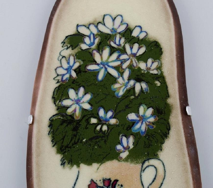 Heljä Liukko-Sundström (geb. 1938) für Arabien. 
Wandtafel aus glasierter Fayence mit handgemalten Blumen. 
Finnisches Design. Datiert 1985.
Maße: 24 x 11,5 cm.
In ausgezeichnetem Zustand.
Unterschrieben.