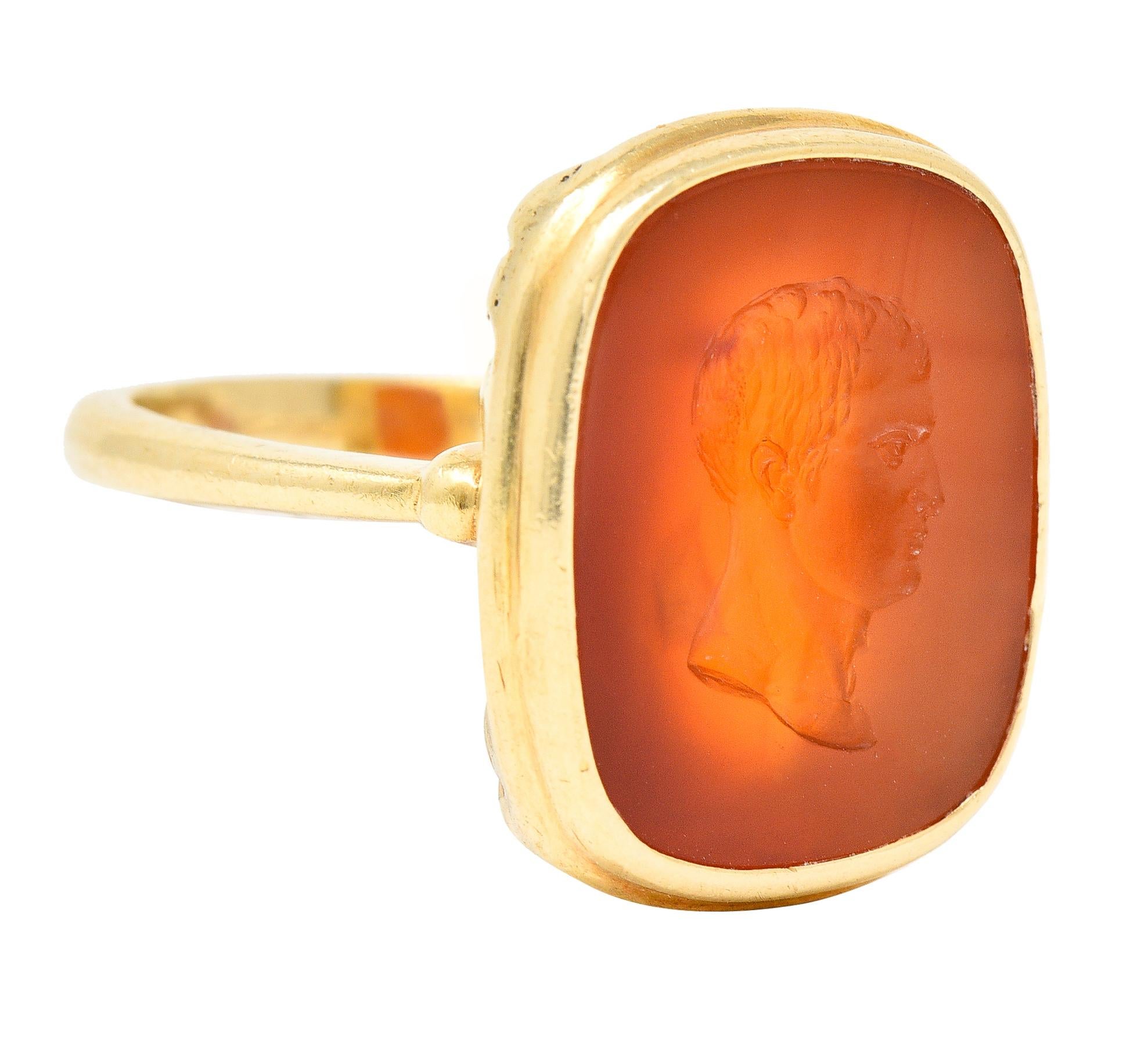 Cushion formed signet ring features a carnelian tablet measuring approximately 7.8 x 4.5 mm. Translucent orangey red in color with very subtle color zoning. Deeply carved to depict the profile of Julius Caesar. Bezel set in a polished gold surround