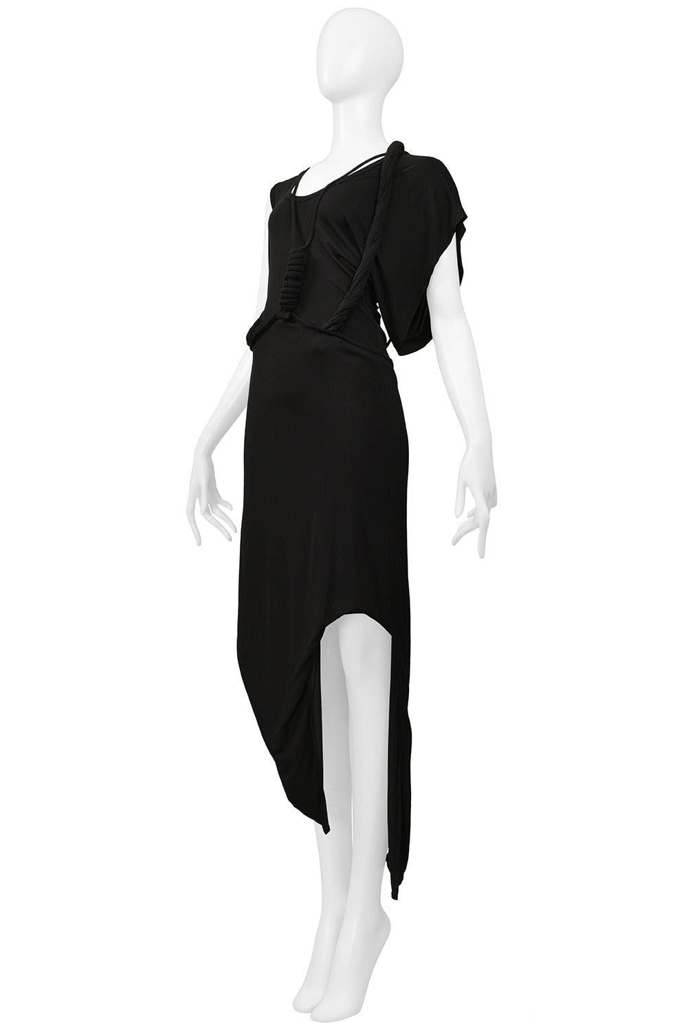 Resurrection Vintage is excited to offer a vintage Helmut Lang black jersey dress featuring an asymmetrical neckline, sleeves, and hem, and decorative cables and knots around the neckline and down the side of the dress, from the 2005 runway