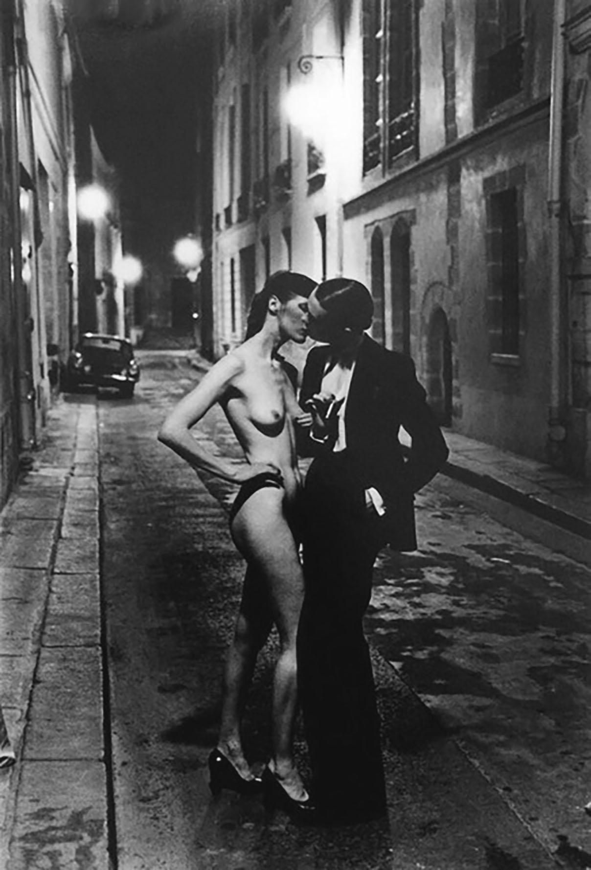 Helmut Newton
s Private Property Collection "Rue Aubriot With Nude Kissing" original fine art shot in 1975, featuring actress, Vibeke Knudsen standing with a nude model in a lamp lit Parisian street. This image is third in the series of one of
