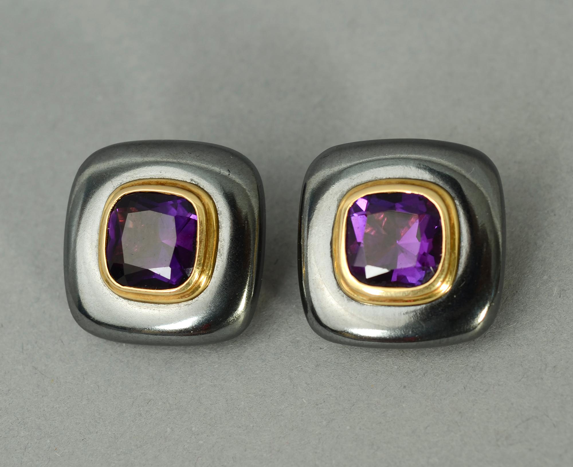 Sporty and sophisticated earrings of a hematite background centered with a gold band within which is a faceted amethyst. The 18 karat earrings have clip backs . Measurements are 3/4 