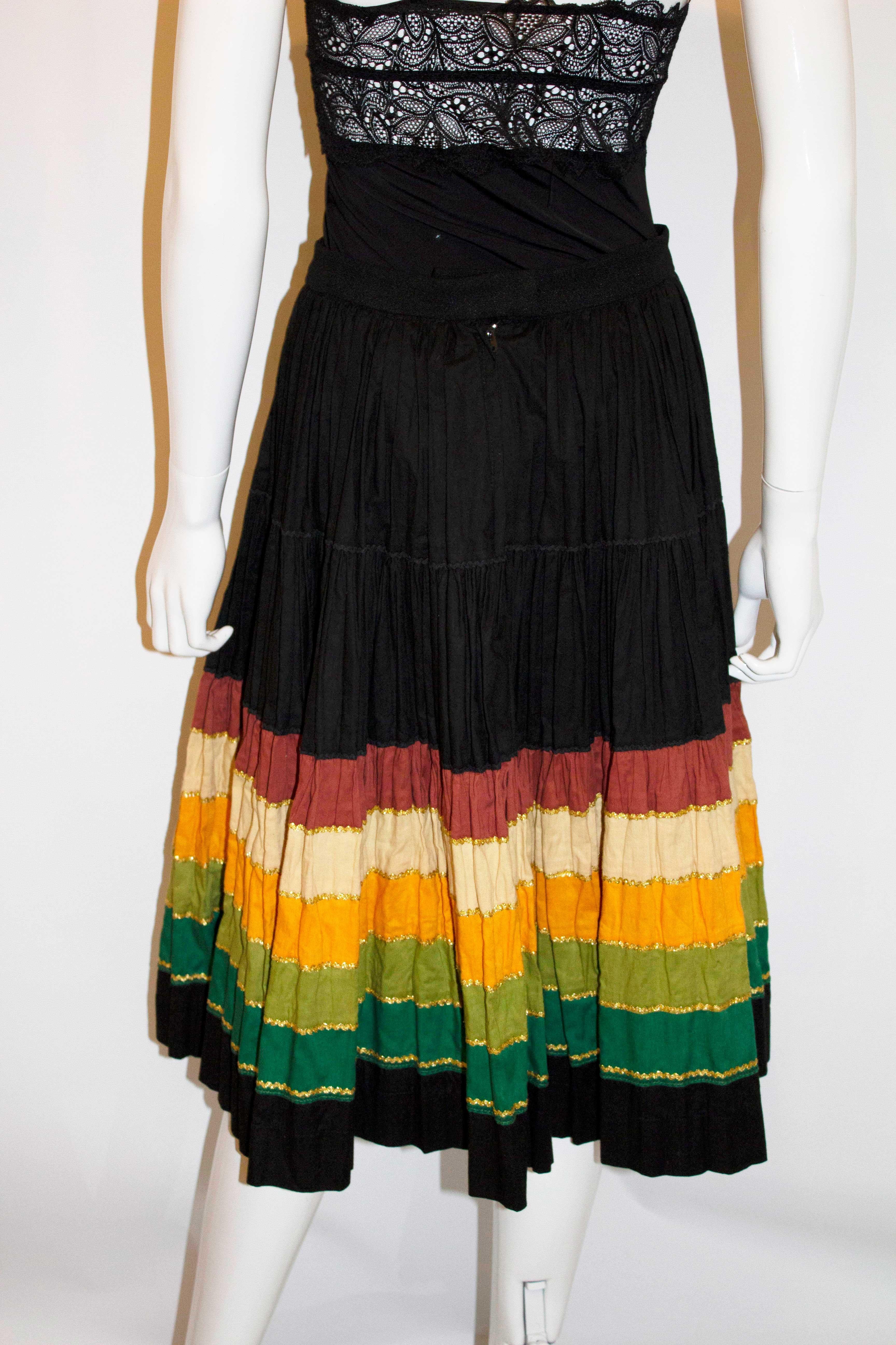 A fun skirt by Hemisphere Paris. The skirt is black with pleats, and colourful and gold braid detail at the hem. Measurements: Waist 28'', length 22''