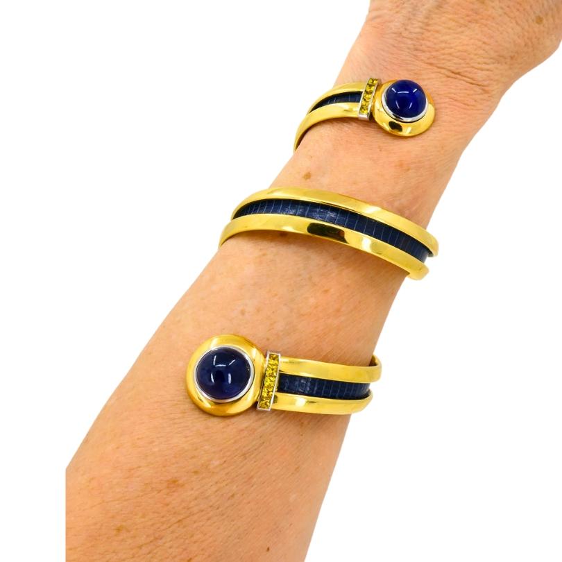 Uno splendido bracciale Hemmerle dal design a spirale, realizzato in oro 18 carati, con zaffiro blu e giallo e intarsi in pelle. 
La forma a spirale aperta avvolge il polso con un senso di movimento dinamico. La finitura oro lucido completa