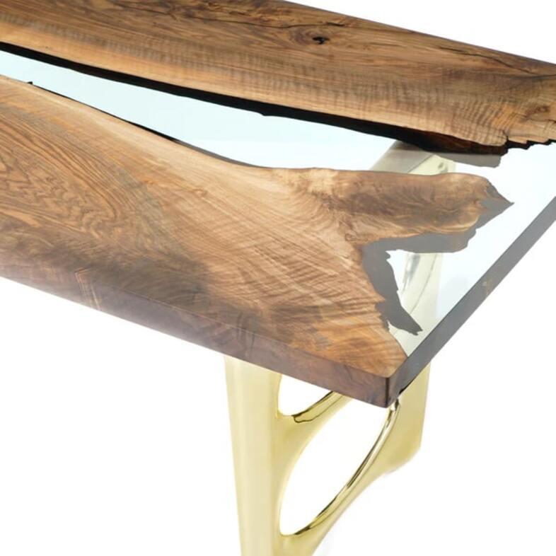 Esta llamativa mesa combina a la perfección la calidez de la madera natural con la elegancia del diseño moderno. La superficie de madera viva, con sus ricos tonos y su textura orgánica, contrasta espectacularmente con un profundo detalle de resina