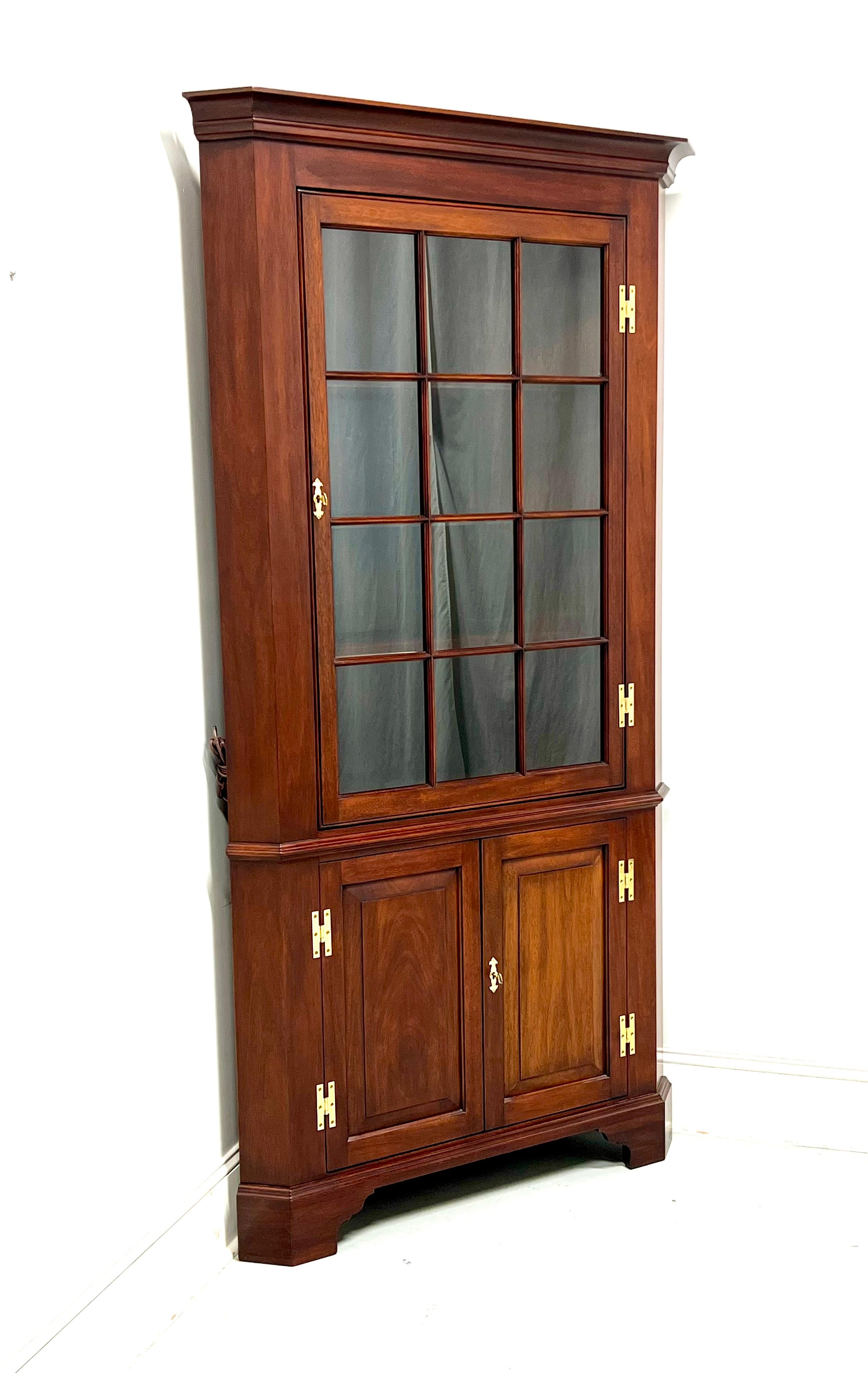 A Chippendale style corner display cabinet by Henkel Harris, their Fairfax. Solid mahogany with brass hardware and bracket feet. Upper lighted cabinet features three fixed wooden shelves with plate grooves behind a lockable single door with 12 glass