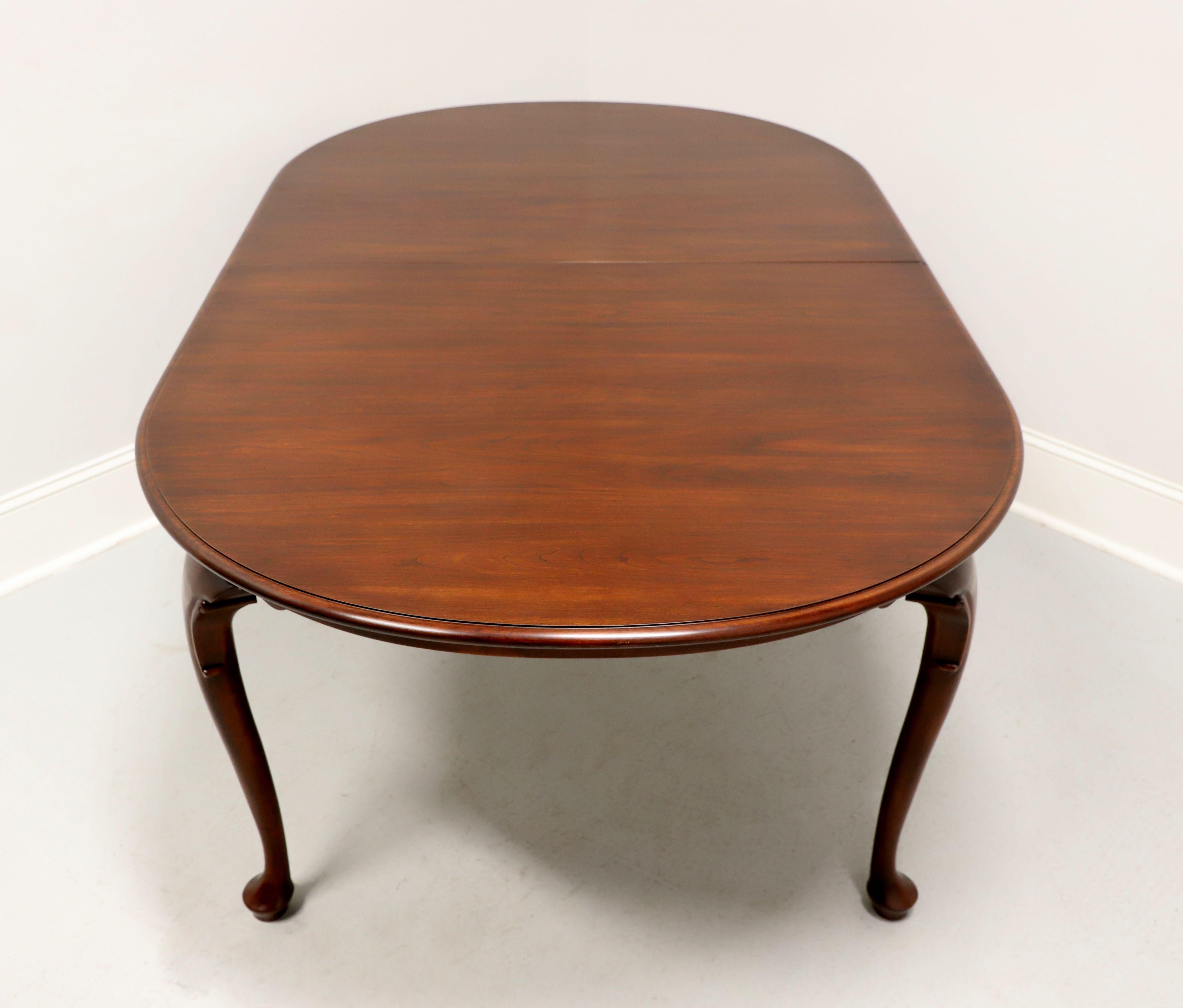 A Queen Anne style oval dining table by Henkel Harris of Winchester, Virginia, USA. Solid wild black cherry wood with bevel edge to the top, carved apron, decoratively carved knees, cabriole legs and pad feet. Includes two 16 inch extension leaves