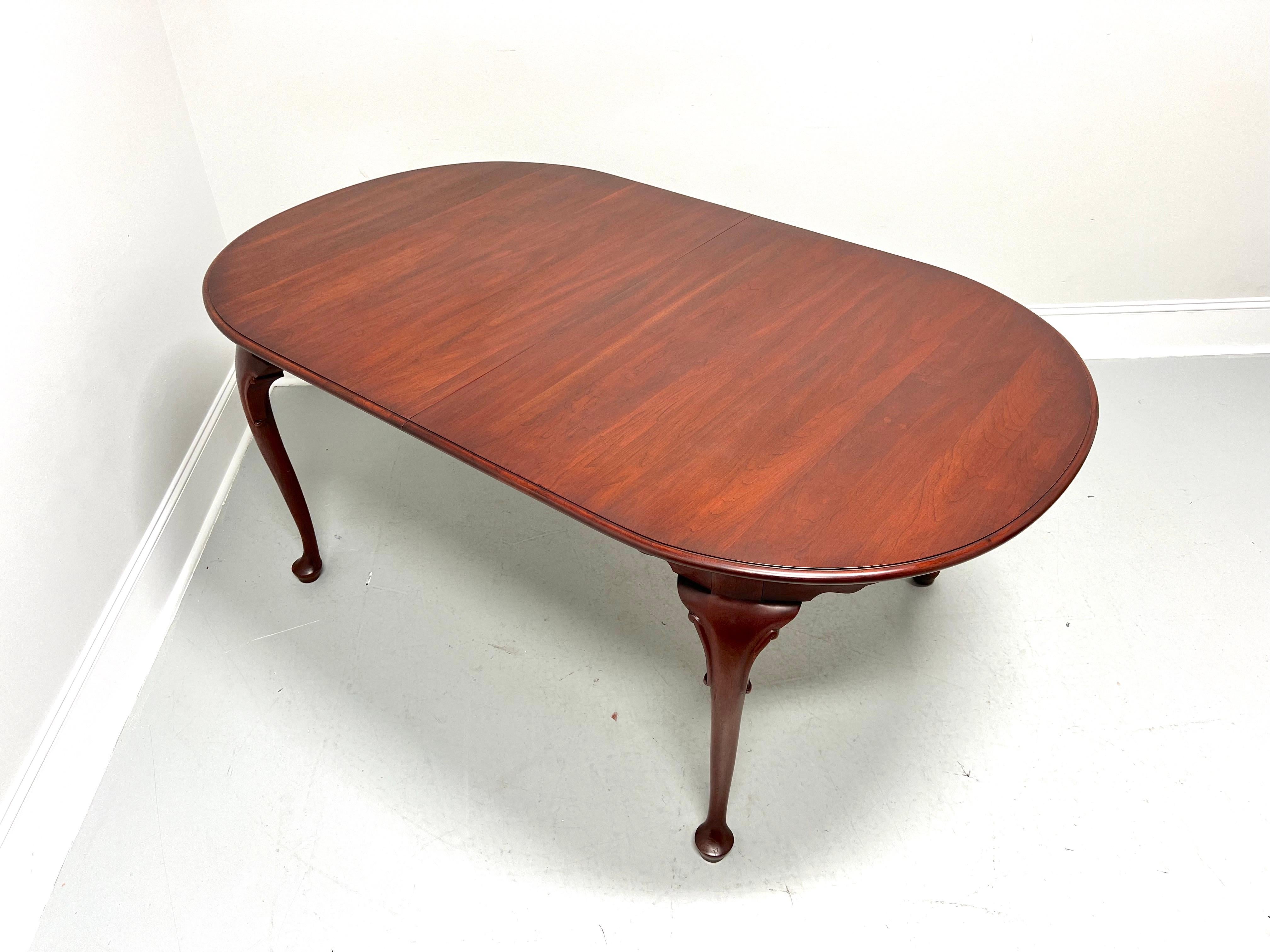 A Queen Anne style oval dining table by Henkel Harris of Winchester, Virginia, USA. Solid wild black cherry wood with bevel edge to the top, carved apron, decoratively carved knees, cabriole legs, and pad feet. Includes two 16 inch extension leaves