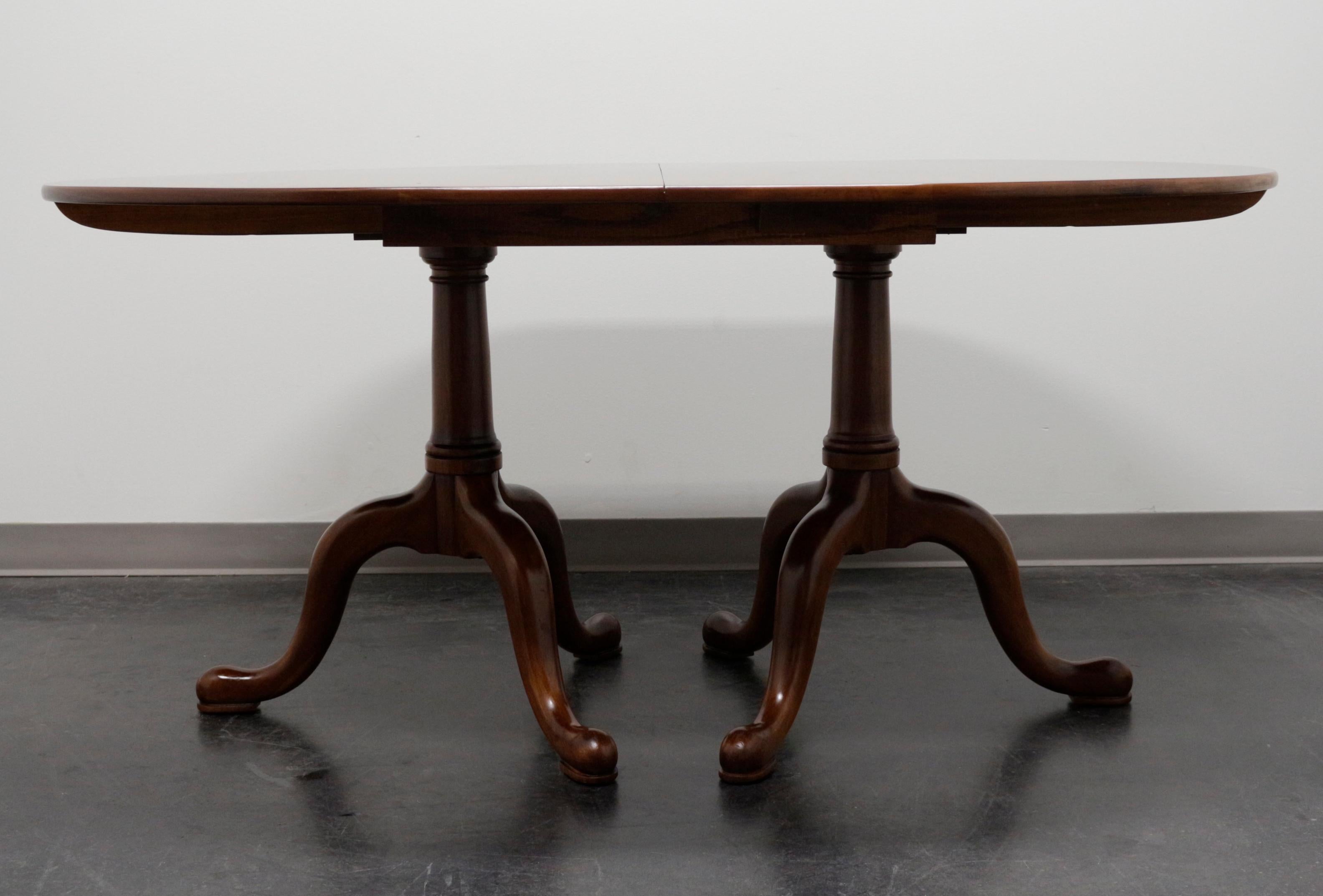 A Queen Anne style dining table by Henkel Harris of Winchester, Virginia, USA. Solid wild black cherry wood with an oval top that sits on two pedestals, each with three curved legs and pad feet. Wood expansion sliders. Includes four extension