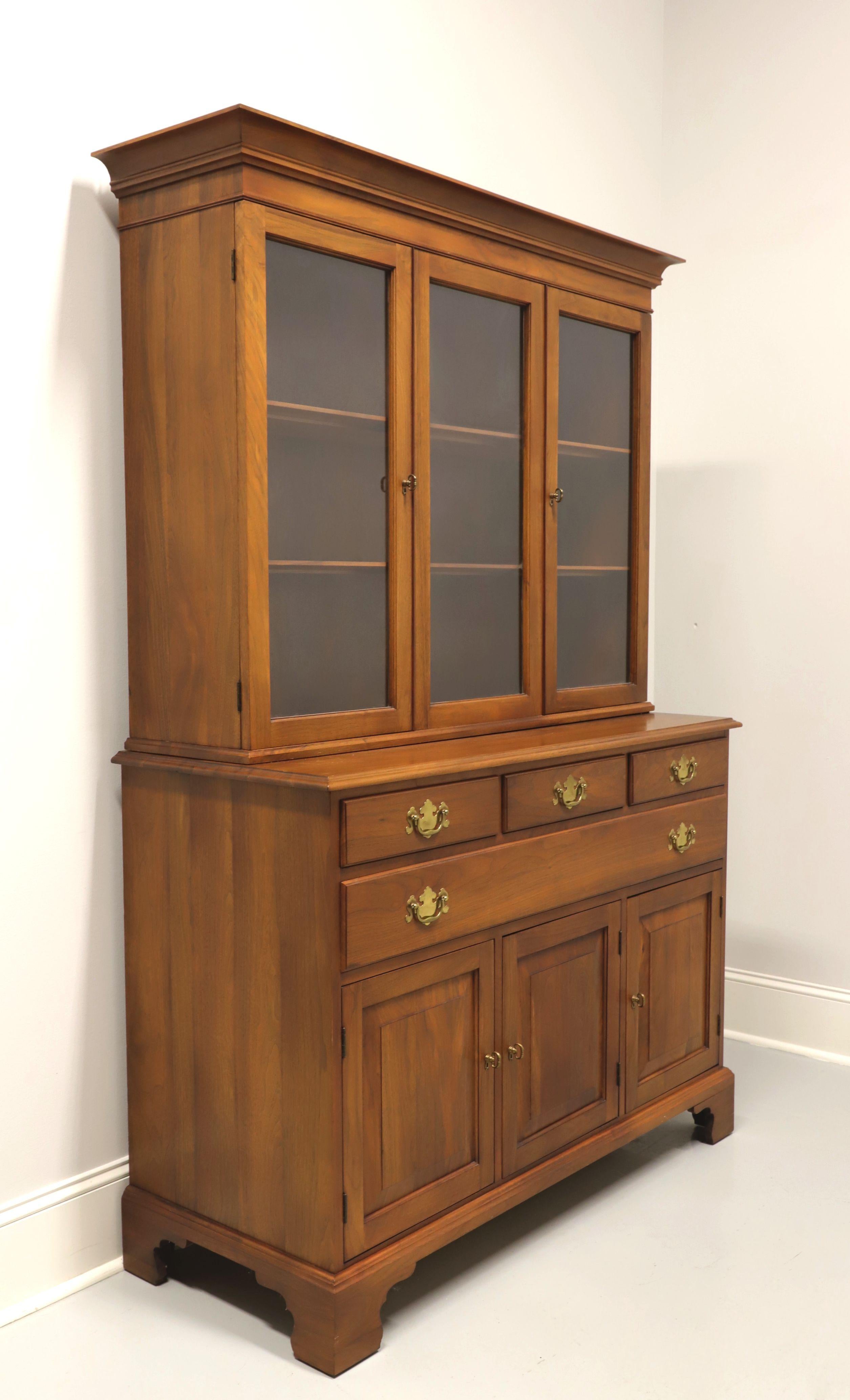 A Colonial style stepback hutch by Henkel Harris, of Winchester, Virginia, USA. Solid walnut with brass hardware, crown molding to top and bracket feet. Upper cabinet features three glass front panes, two of which are doors, center being stationary,