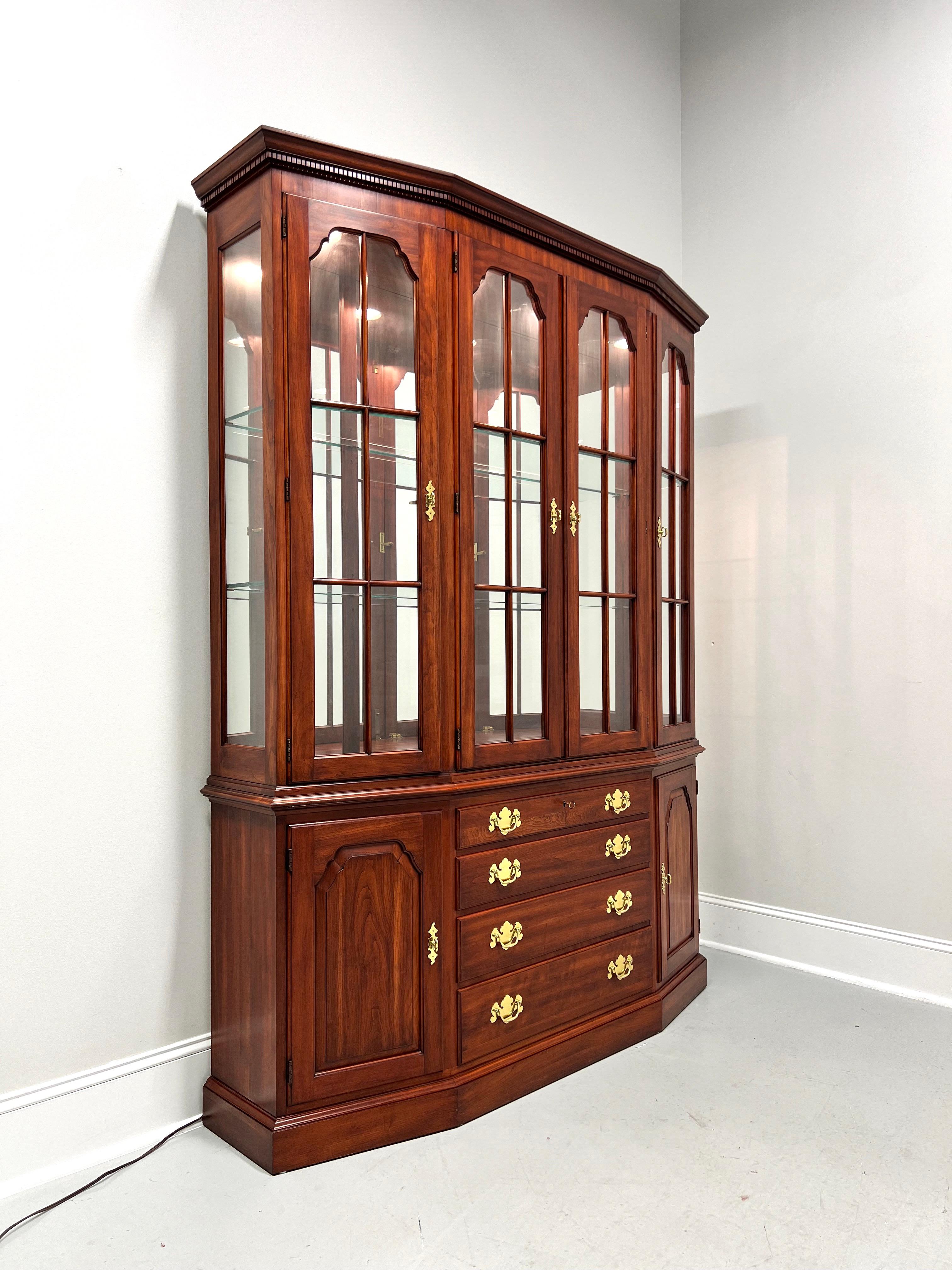 A Traditional style china cabinet by Henkel Harris, of Winchester, Virginia, USA. Solid wild black cherry wood, canted shape, brass hardware, crown & dentil molding at top, ogee edge to lower cabinet, and a solid base. Upper cabinet has four