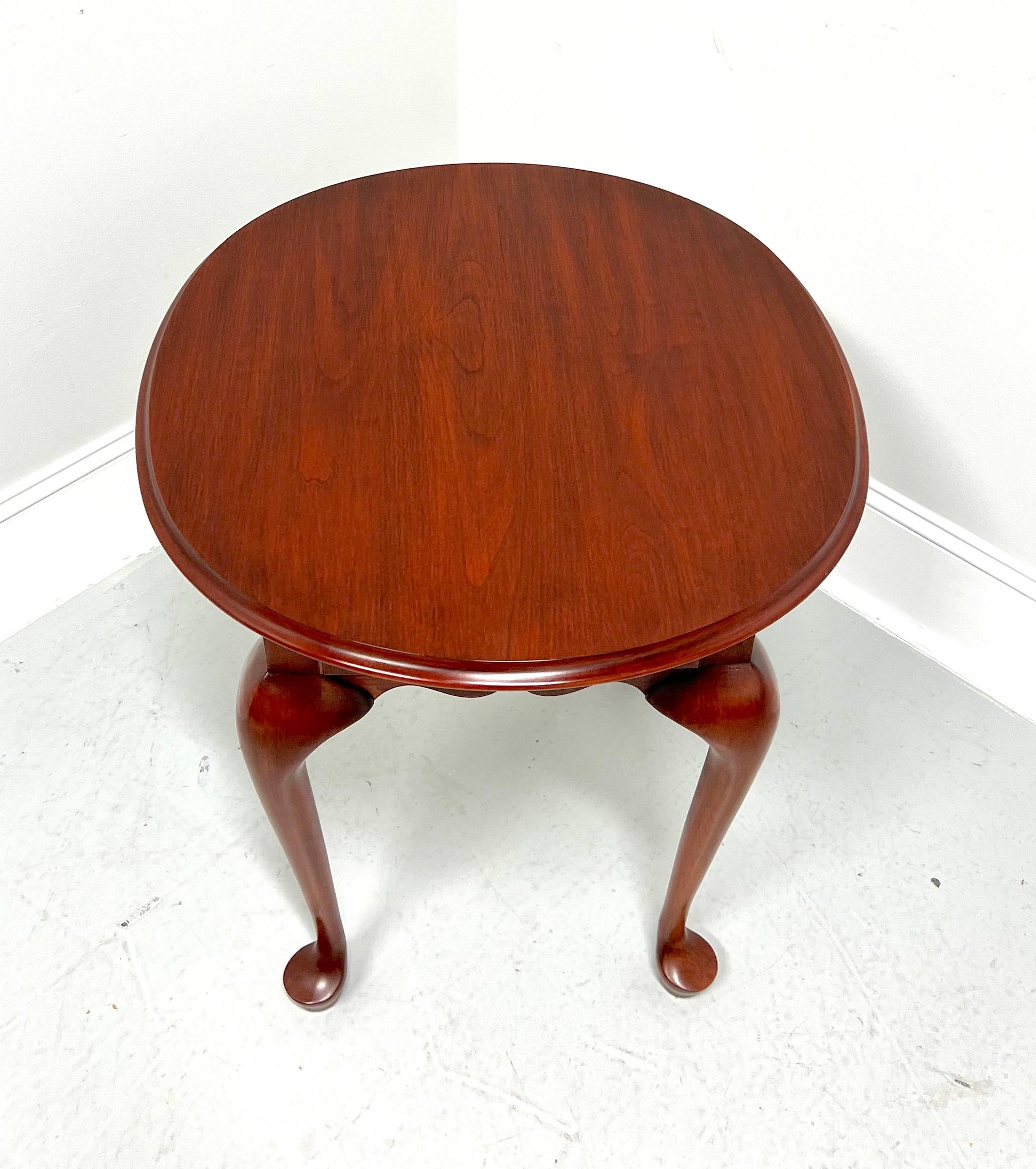 A Queen Anne style oval end side table by Henkel Harris, of Winchester, Virginia, USA. Solid wild black cherry wood with brass hardware, bevel edge to the top, carved apron, cabriole legs, and pad feet. Features one drawer of dovetail construction.
