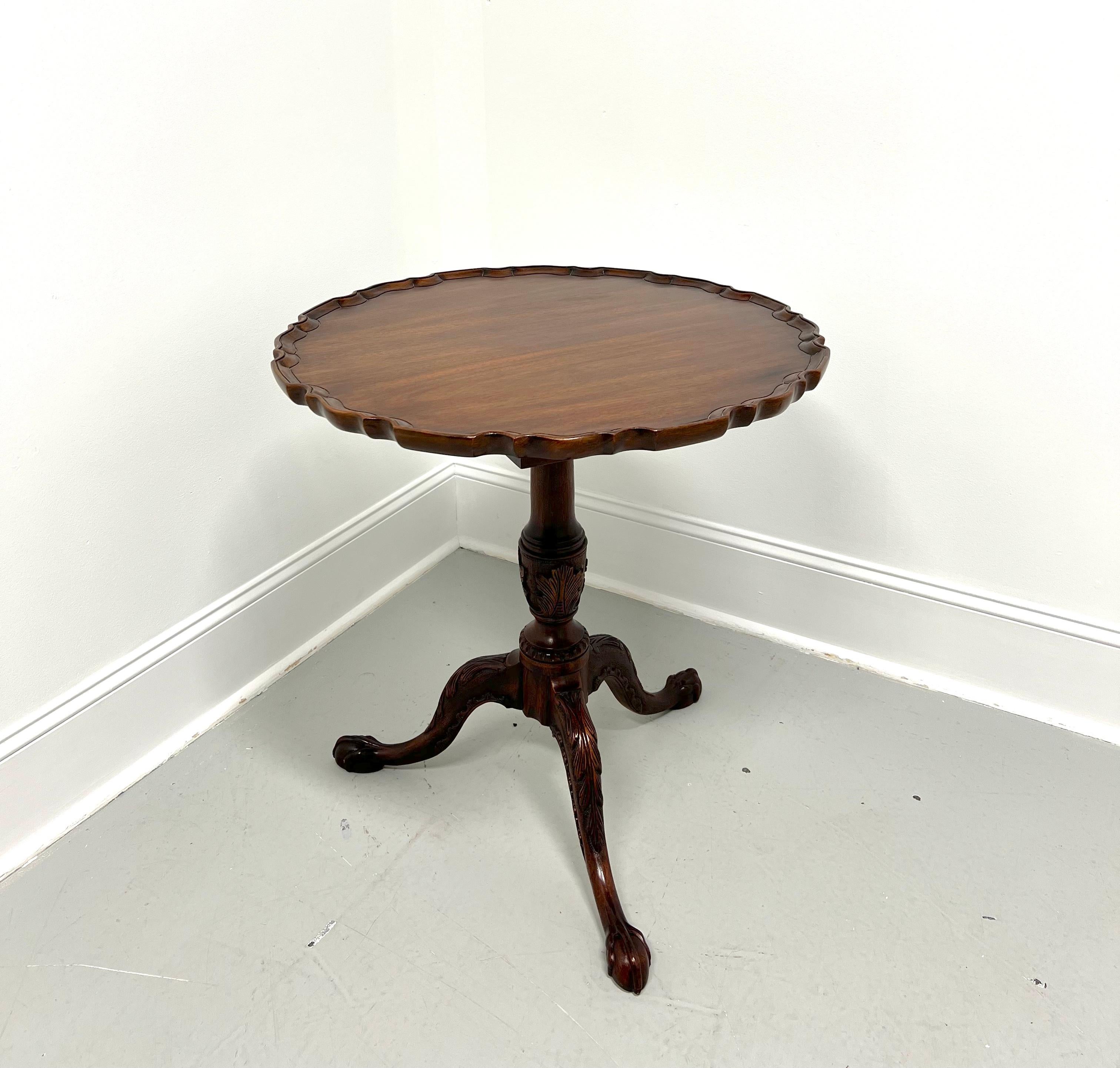 A Chippendale style tilt-top pie crust table by Henkel Harris, of Winchester, Virginia, USA. Solid mahogany with scalloped edge top, tilt mechanism, brass latch, acanthus leaf carved pedestal with birdcage top, three legs with acanthus leaf carved