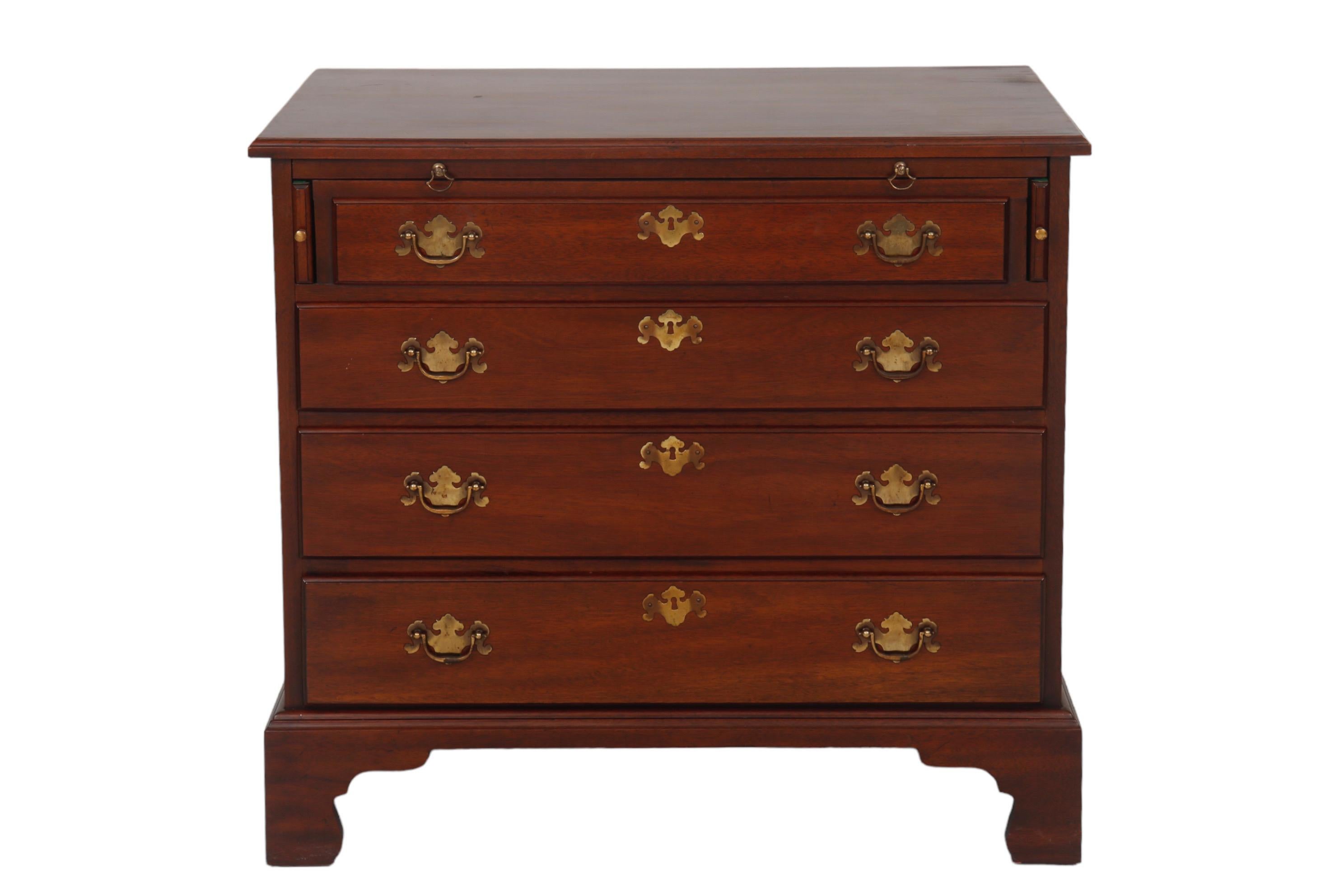 A Chippendale style bachelor chest in mahogany, made by Henkel-Harris of Winchester, Virginia. A top pull-out shelf rests on slides at each side with knob handles. Four dovetailed drawers open with brass bail handles on bat shaped back plates.