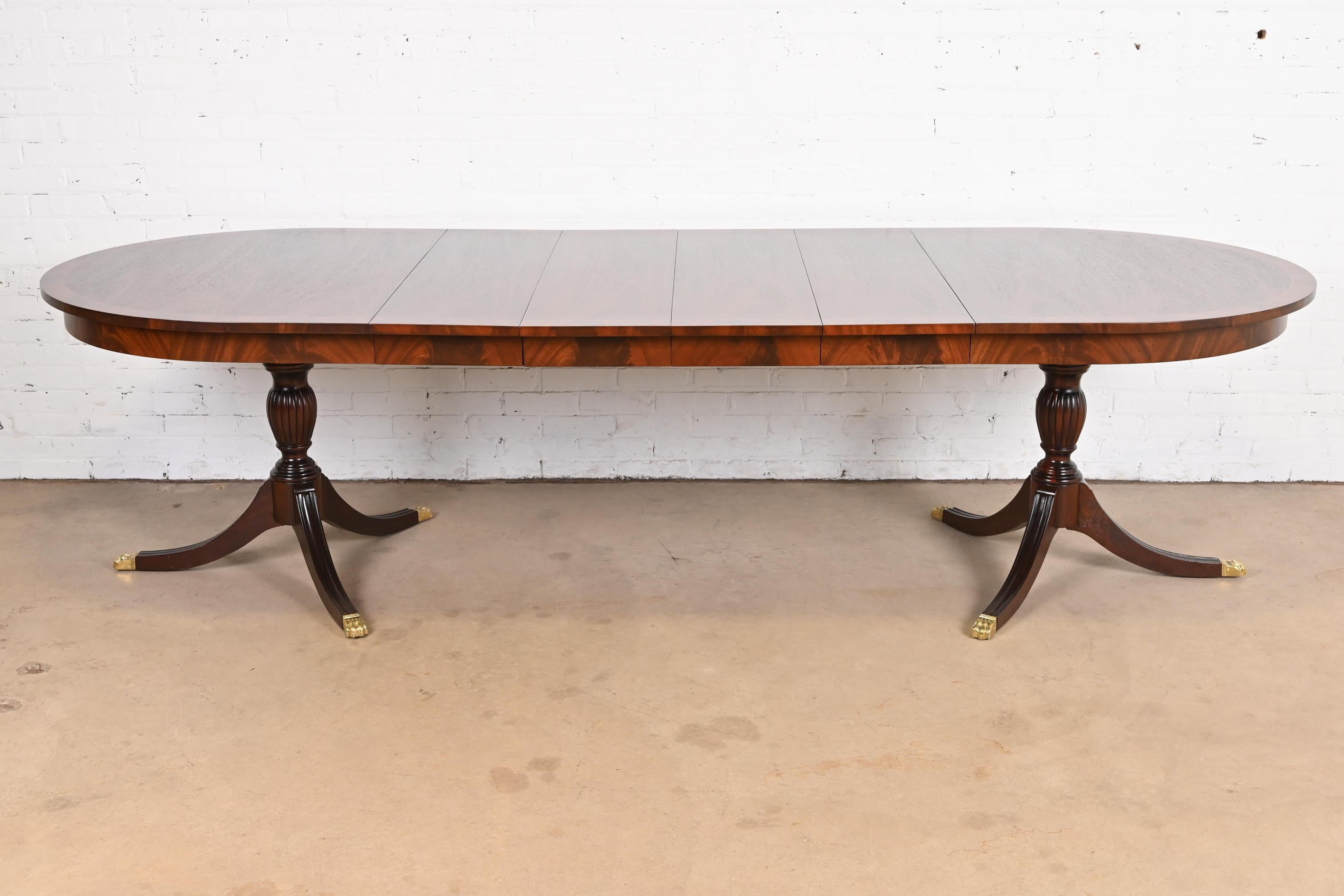 An exceptional Georgian or Regency style double pedestal extension dining table

By Henkel Harris

USA, Circa 1980s

Book-matched mahogany, with satinwood string inlay and flame mahogany banding, carved mahogany pedestals, and brass capped paw