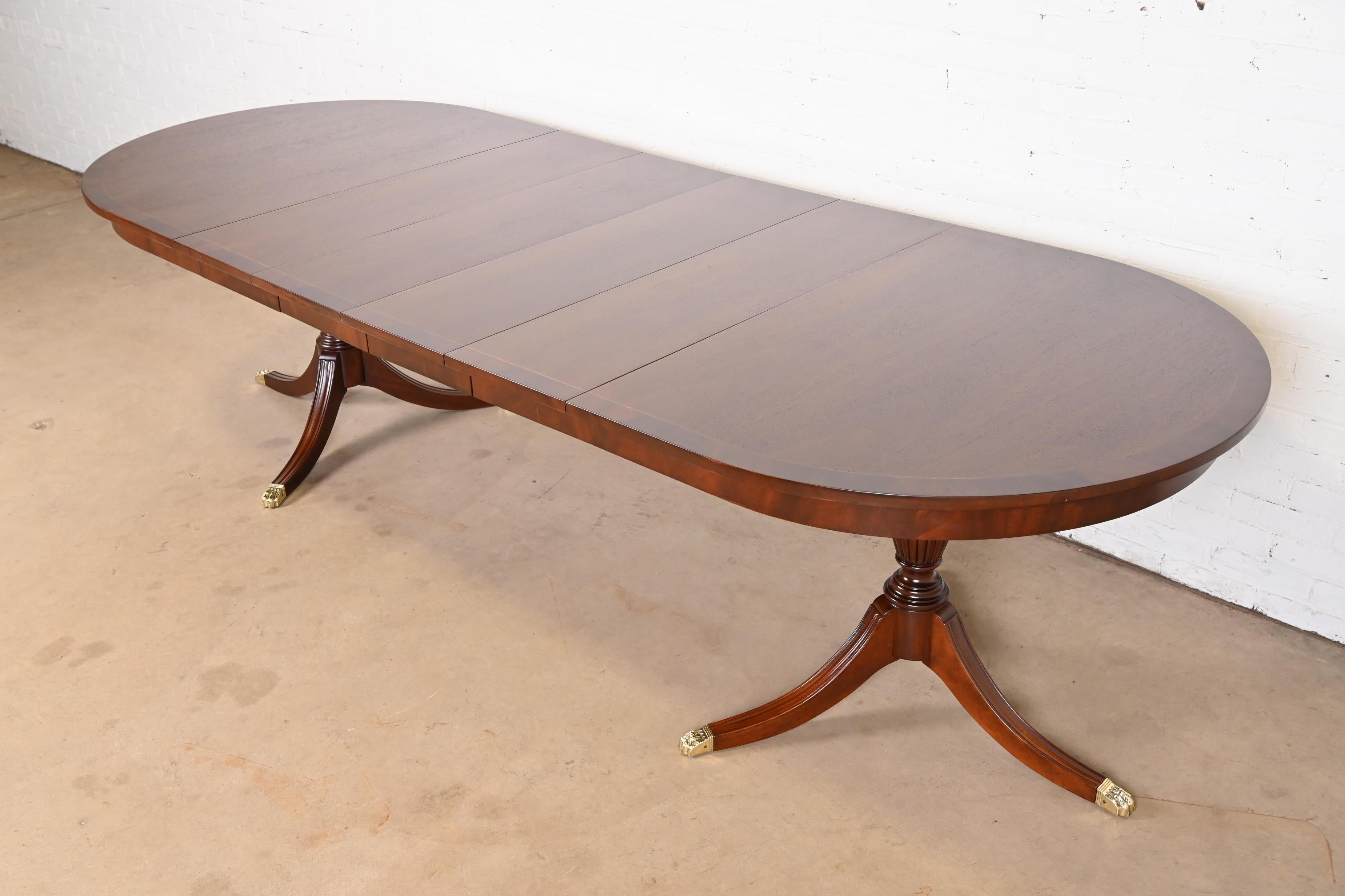 An exceptional Georgian or Regency style double pedestal extension dining table

By Henkel Harris

USA, Circa 1980s

Book-matched mahogany, with satinwood string inlay and flame mahogany banding, carved mahogany pedestals, and brass capped paw