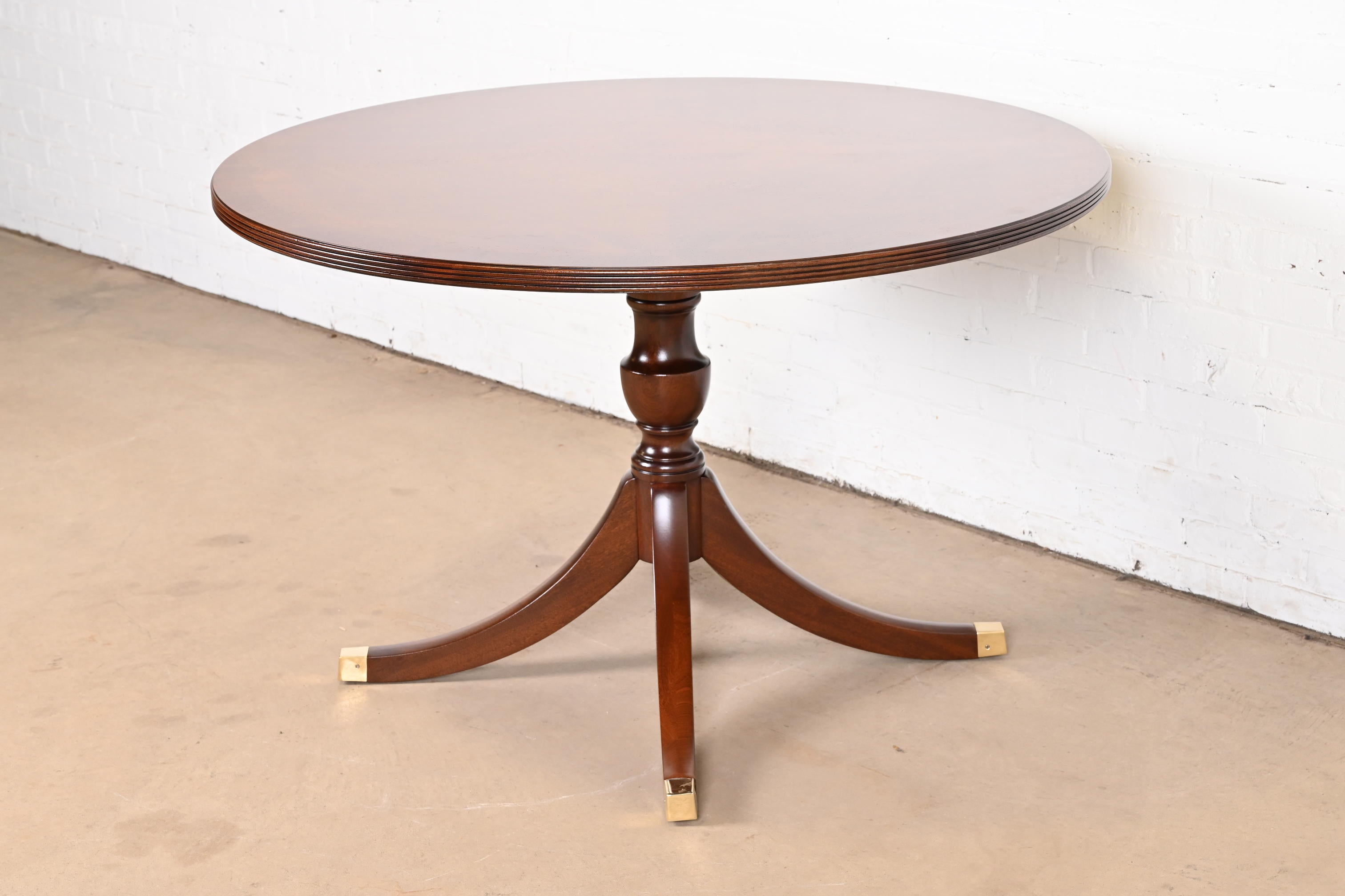An exceptional Georgian or Regency style pedestal dining table, center table, or breakfast table

By Henkel Harris

USA, 2006

Gorgeous book-matched banded mahogany, with carved solid mahogany pedestal and brass-capped feet.

Measures: 48