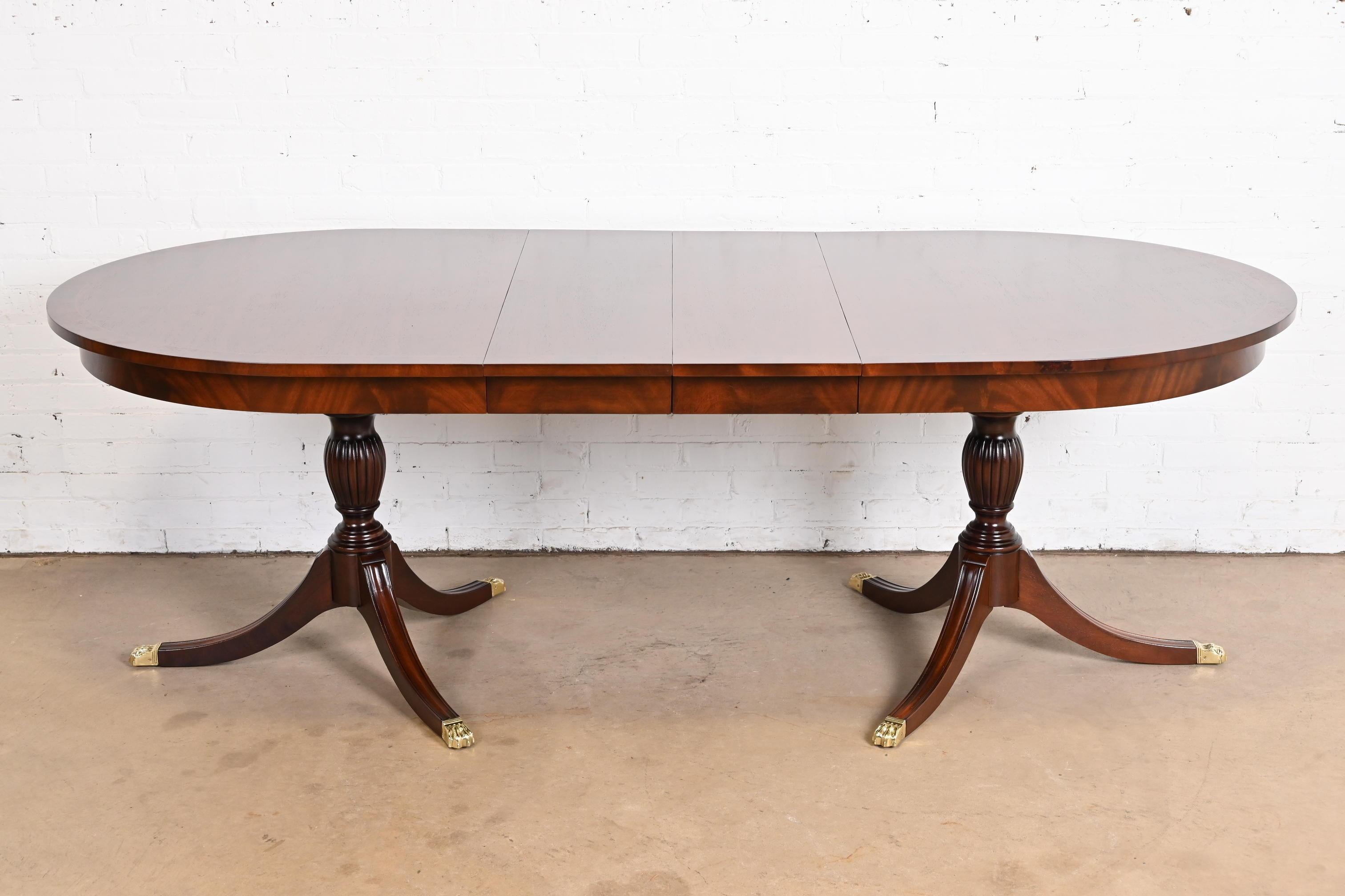 An exceptional Georgian or Regency style double pedestal extension dining table

By Henkel Harris

USA, 1980s

Gorgeous book-matched mahogany top, with satinwood string inlay, solid carved mahogany pedestals, and brass-capped paw feet.

Measures: