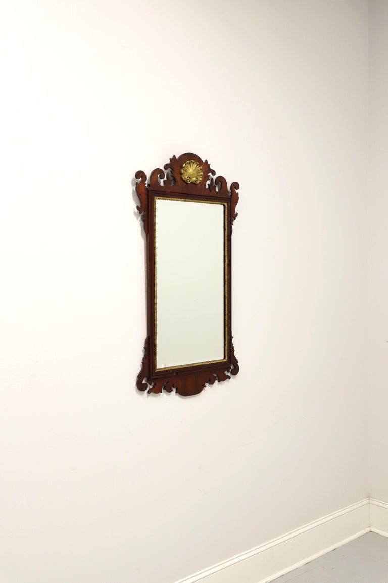 A Chippendale style wall mirror by Henkel Harris, of Winchester, Virginia, USA. Bevel edge mirrored glass, flame mahogany frame with gold trim and top center gold gilt shell shaped medallion. Made circa 1994.

Style #: H-5, Finish #: 29

Measures: