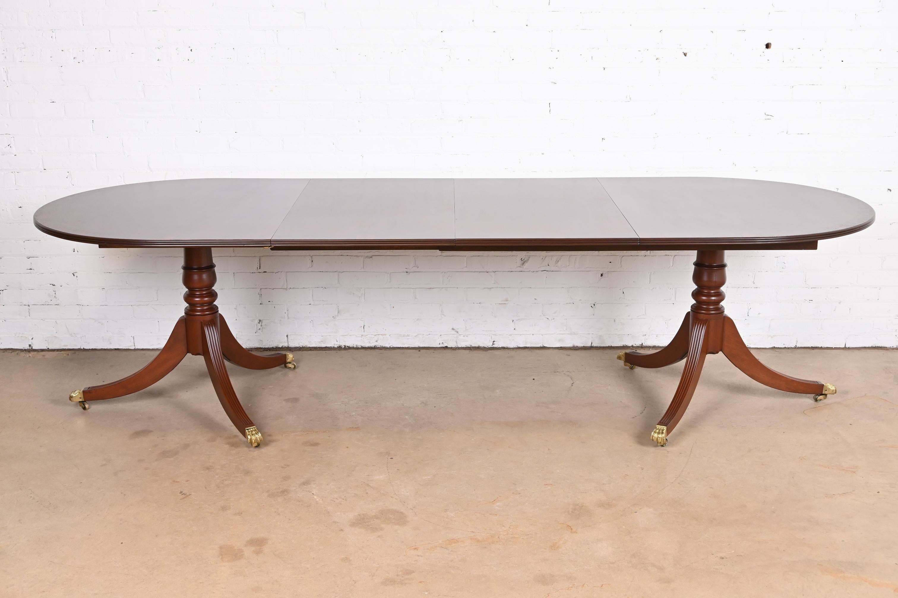An exceptional Georgian or Regency style double pedestal extension dining table

In the manner of Henkel Harris

USA, Circa 1960s

Gorgeous mahogany, with rosewood banding, carved mahogany pedestals, and brass-capped paw feet on casters.

Measures: