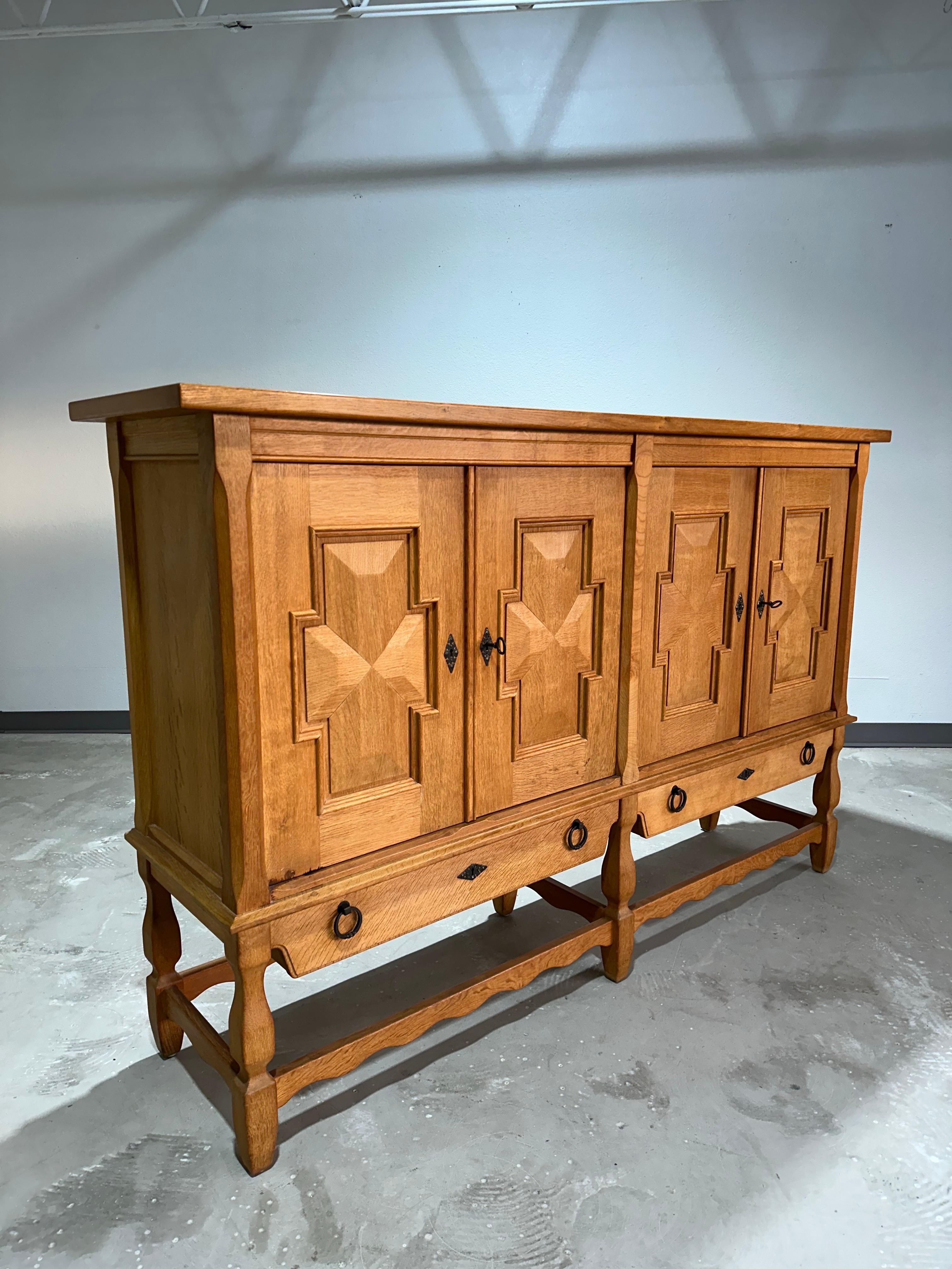 Danish solid oak brutalist highboard c1970’s attributed to Henning Kjaernulf. Four door with carved detailing and two lower drawers, all locking with two included keys. Doors on right reveal open shelving, doors on left open to reveal four shallow