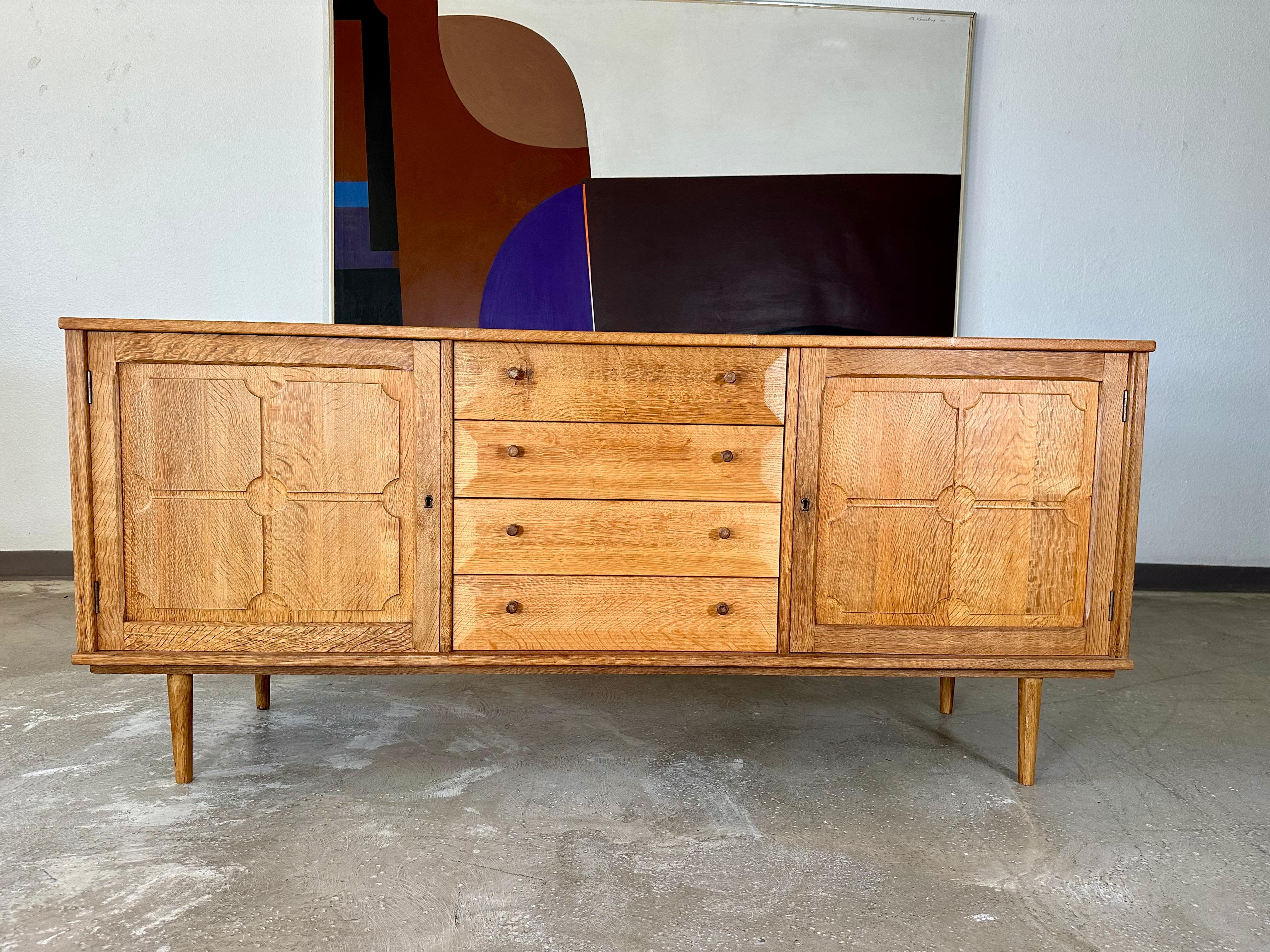 Vintage Danish solid oak brutalist sideboard credenza c1970’s attributed to Henning Kjaernulf. Carved panels on locking doors at left and right open to one felt lined drawer and one shelf in each side. Center features four bevel edge drawers with