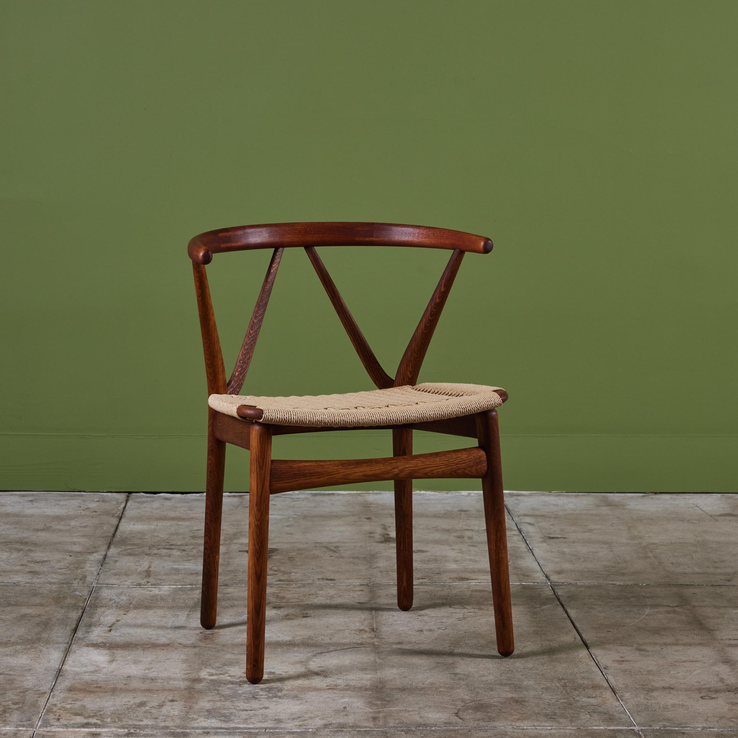 Dining chair from Henning Kjaernulf, produced by Bruno Hansen. Constructed in teak and oak, with a woven paper cord seat and a curved backrest with angled supports, reminiscent of Hans Wenger’s “Wishbone” chair. The chair rests on four rounded legs