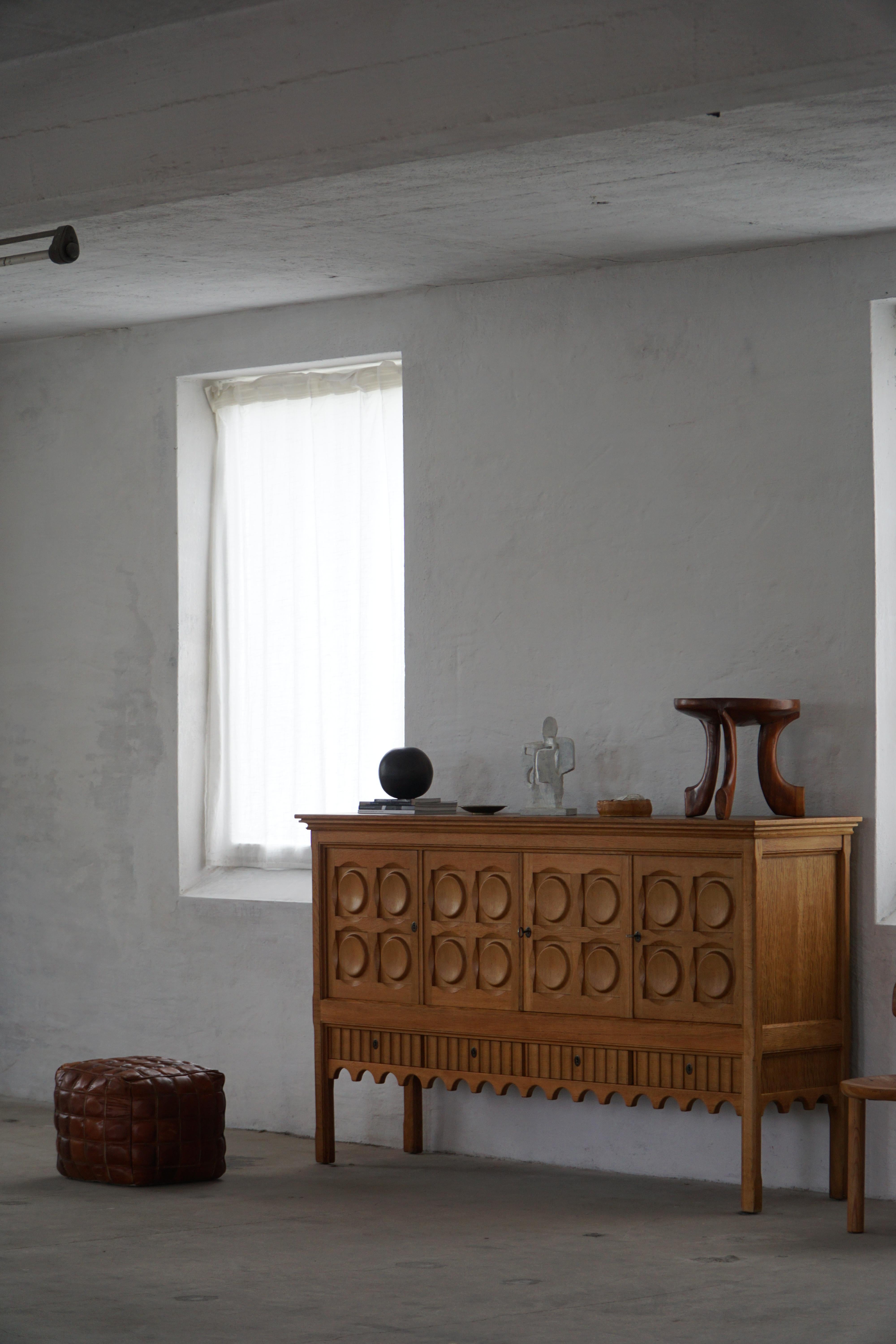 Una bellissima credenza rettangolare in rovere massiccio che offre un ampio spazio di archiviazione e un fronte splendidamente intagliato con dettagli scultorei. Disegnato da Henning Kjærnulf per la Nyrup Møbelfabrik negli anni '60, questo pezzo