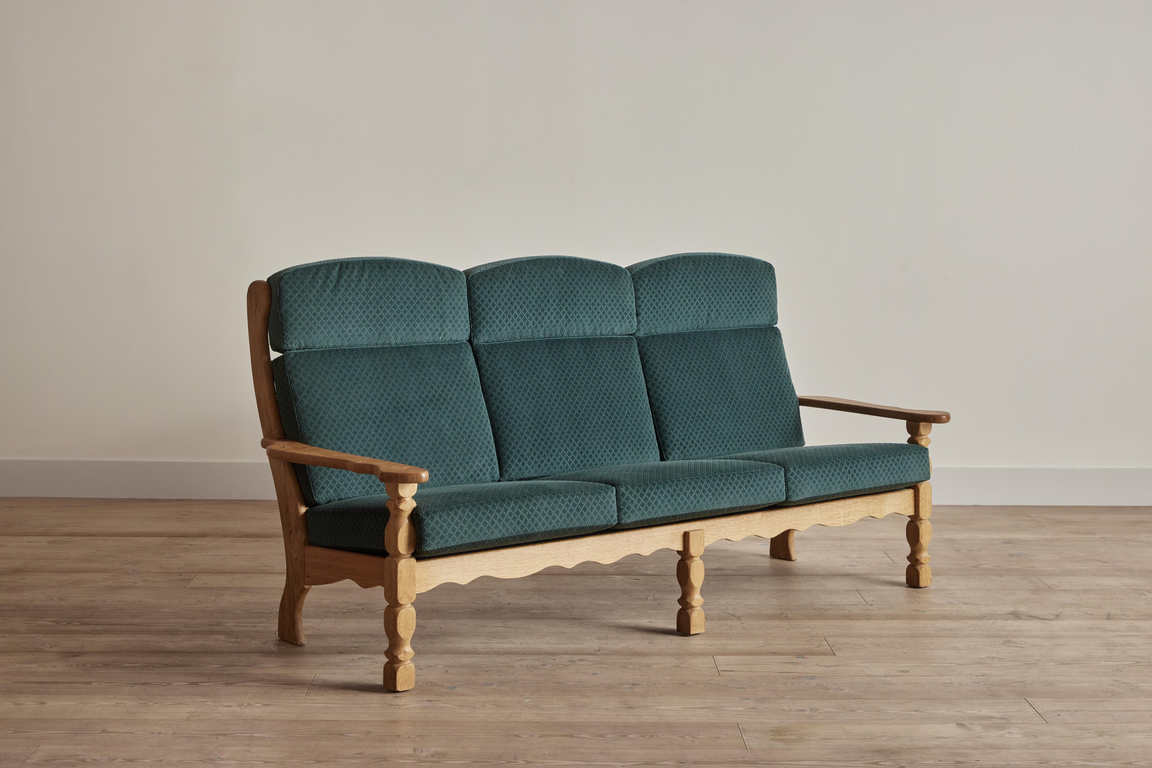 Carved oak wood sofa attributed to Danish designer Henning Kjaernulf. This 1960s sofa has been reupholstered in George Spencer's Clarence fabric in Twilight. Wood frame has been cleaned and waxed. Some wear on wood that is consistent with age and