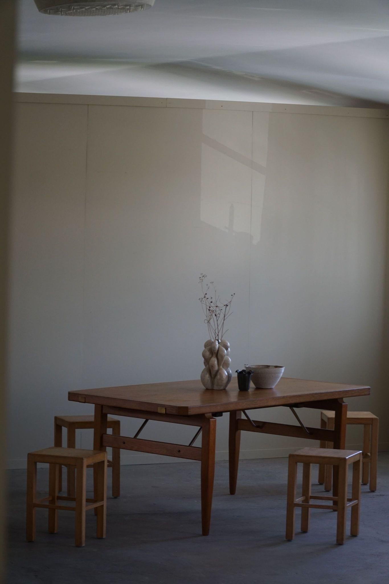 This rectangular dining table, designed by Henning Kjærnulf in the 1960s, showcases classic Danish mid-century style. Crafted from oak, it features elegant brass details that add a touch of sophistication. The clean lines and functional design make