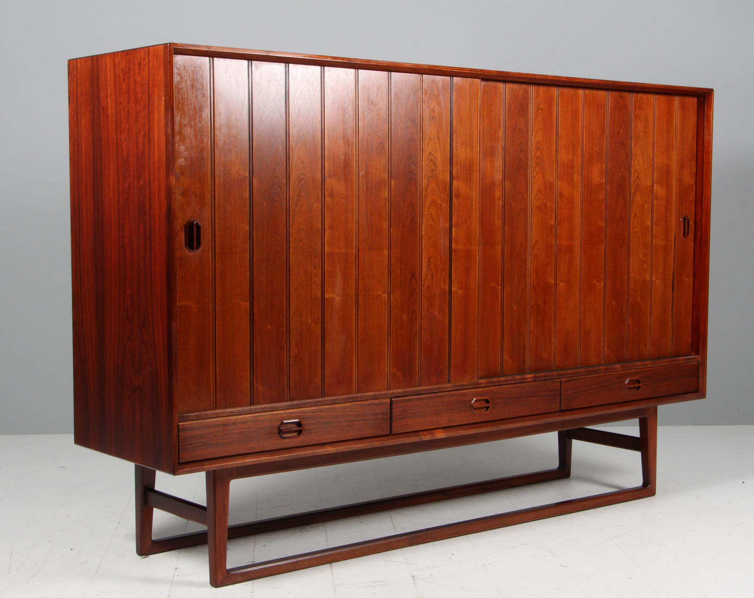 Credenza Henning Kjærnulf in palissandro. I cassetti e le ante si trovano dietro gli scaffali.

Prodotto da Sibast.