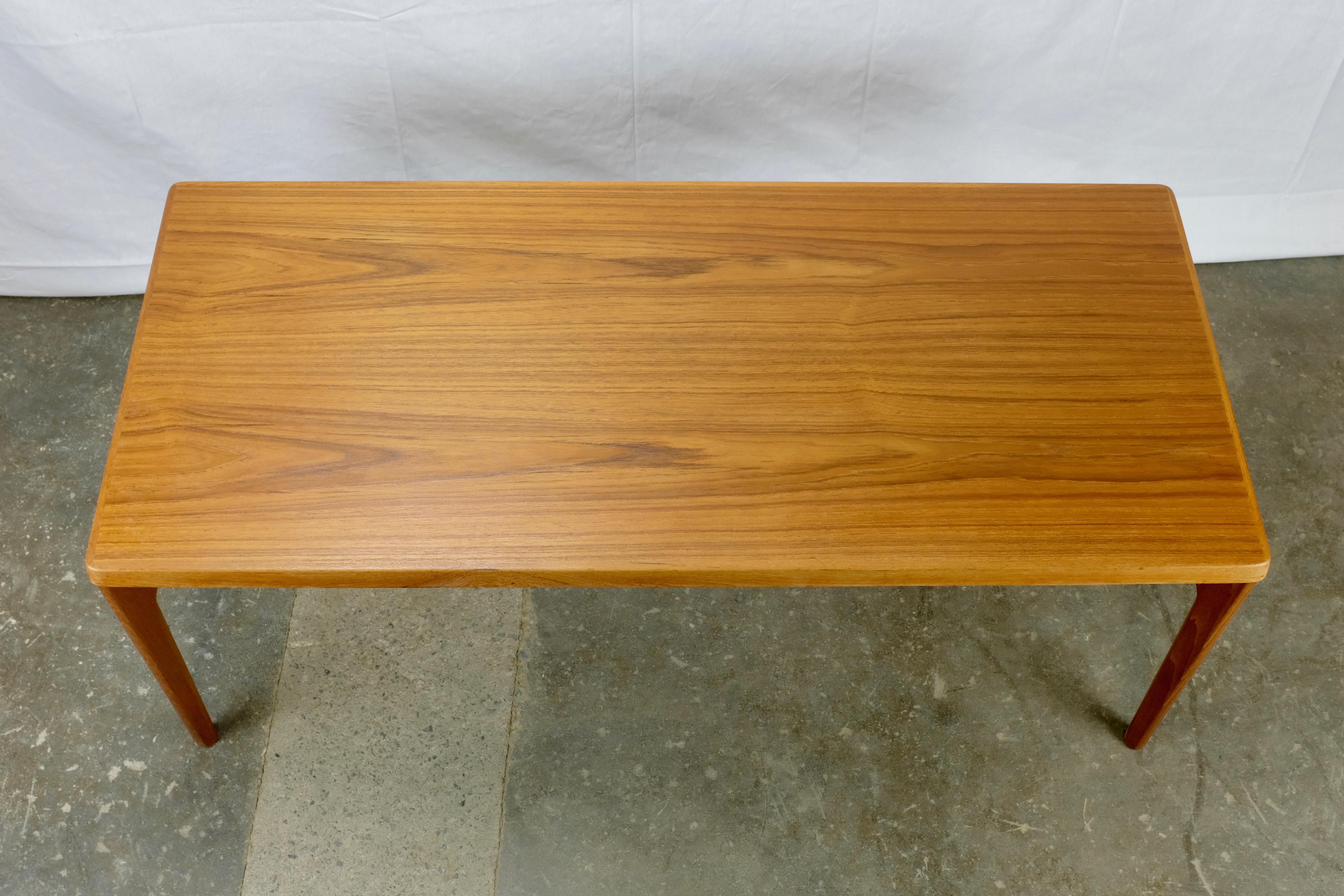 Coffee table designed by Henning Kjaernulf and made in Denmark by Vejle Stole og Møbelfabrik.

The top is teak veneer with a thick solid teak edge featuring a downward-sloping bevel. The legs and aprons are solid teak. Manufacturer's stamp on