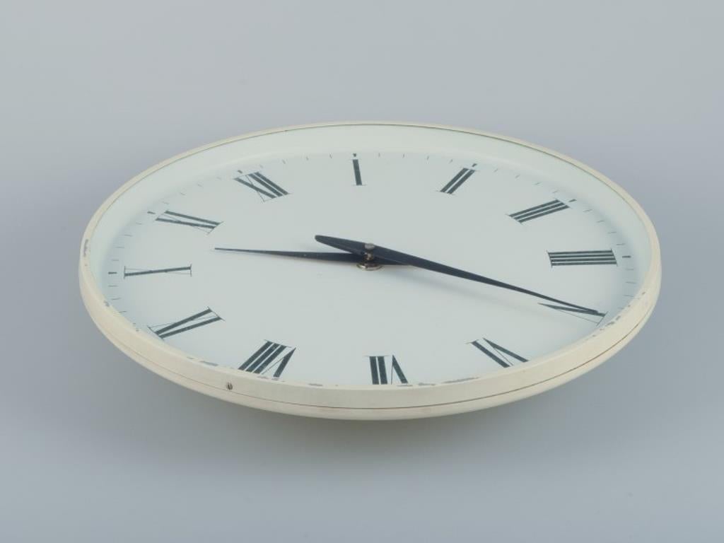 Henning Koppel for Georg Jensen. 
Wall clock made of white plastic and metal. 
Dial with Roman numerals and hands.
1960s/70s.
Diameter: 40 cm.
In good condition with signs of use.
Dimensions: D 39.5 cm x D 8.0 cm.